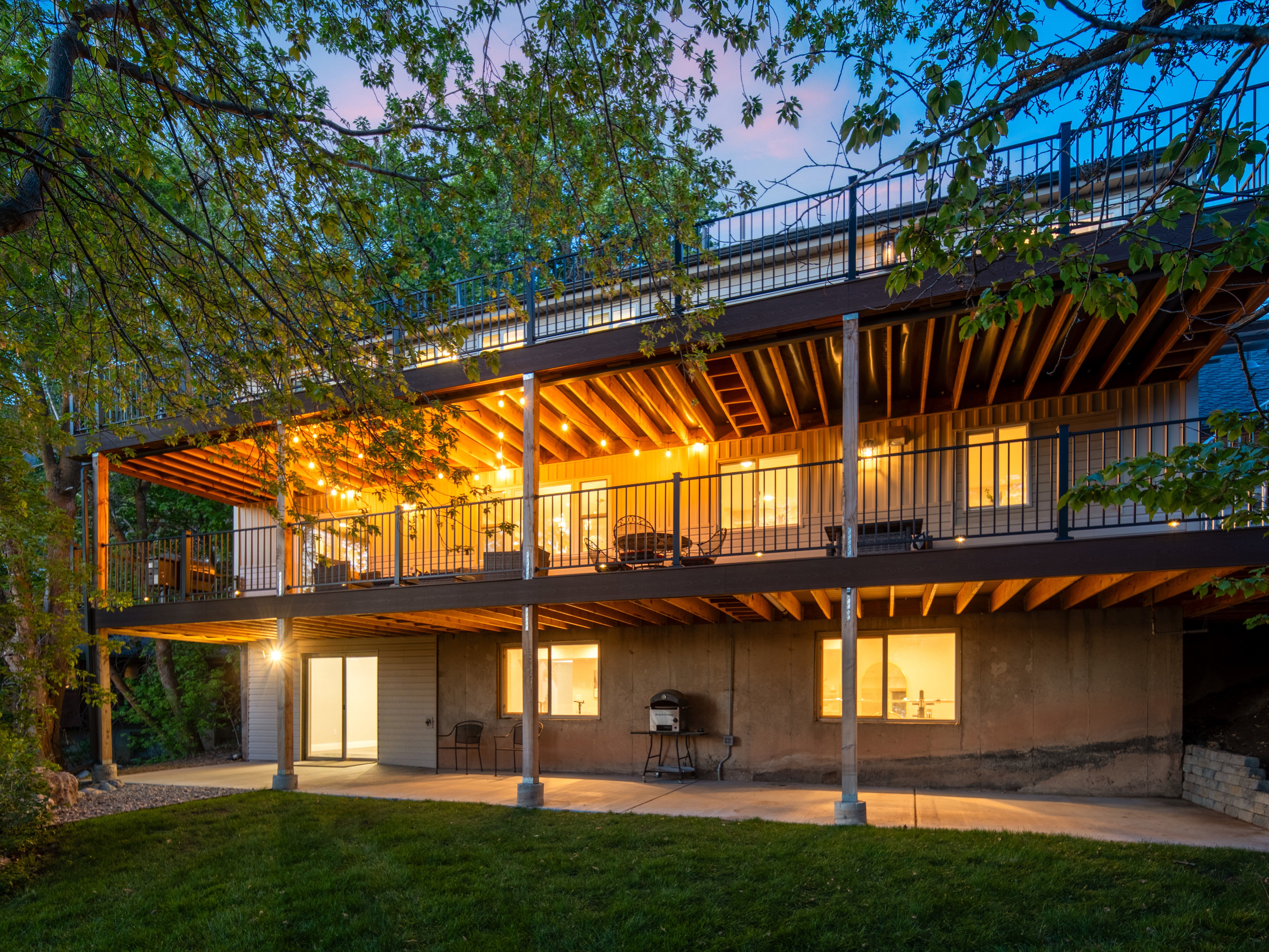 Multi-level rear exterior featuring a ground-level patio, two expansive decks with black railings, and a walk-out basement with sliding glass doors
