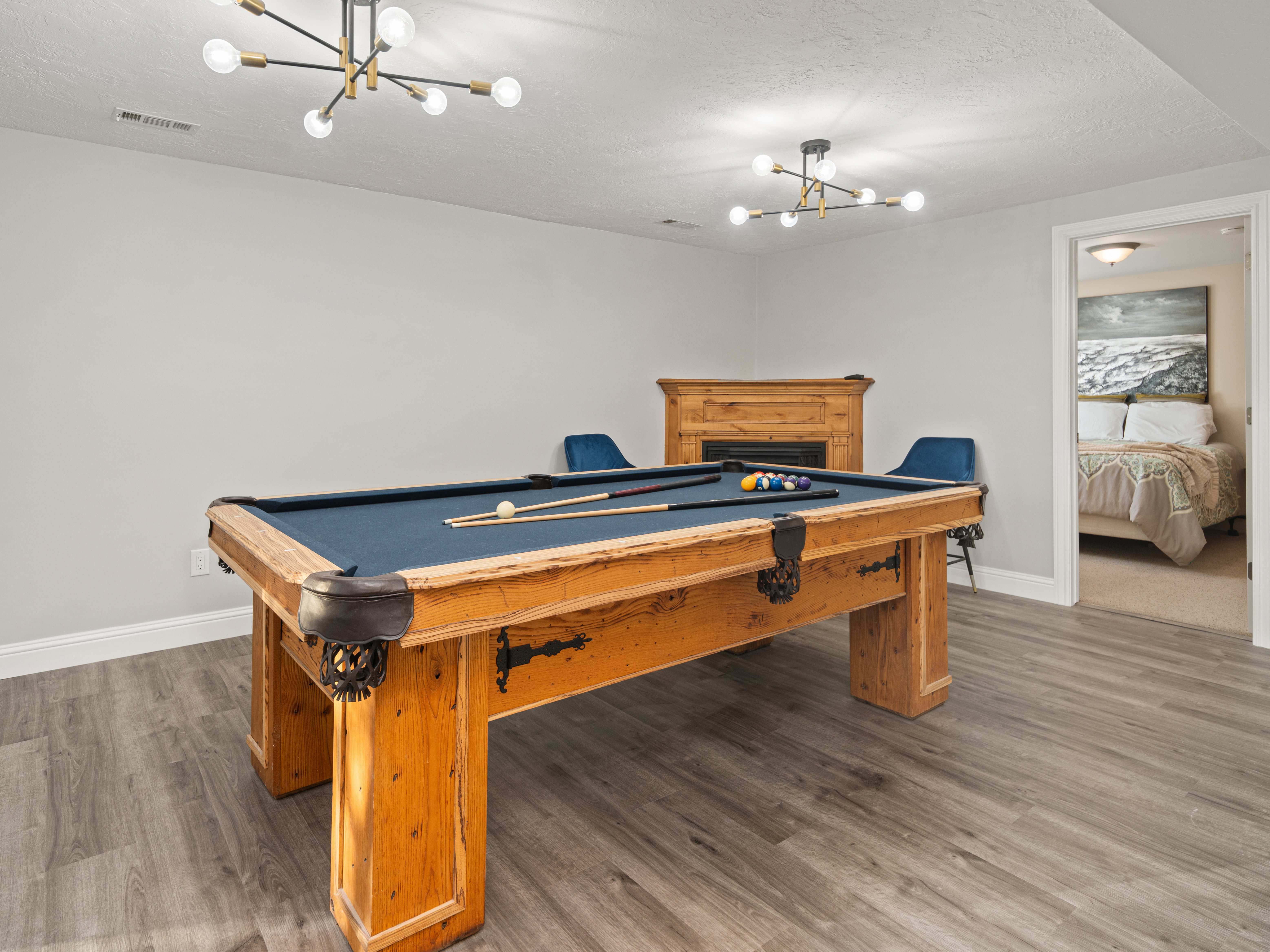 Recreation room featuring a pool table, modern sputnik chandeliers, wood-finish flooring, and a fireplace with a wood mantel