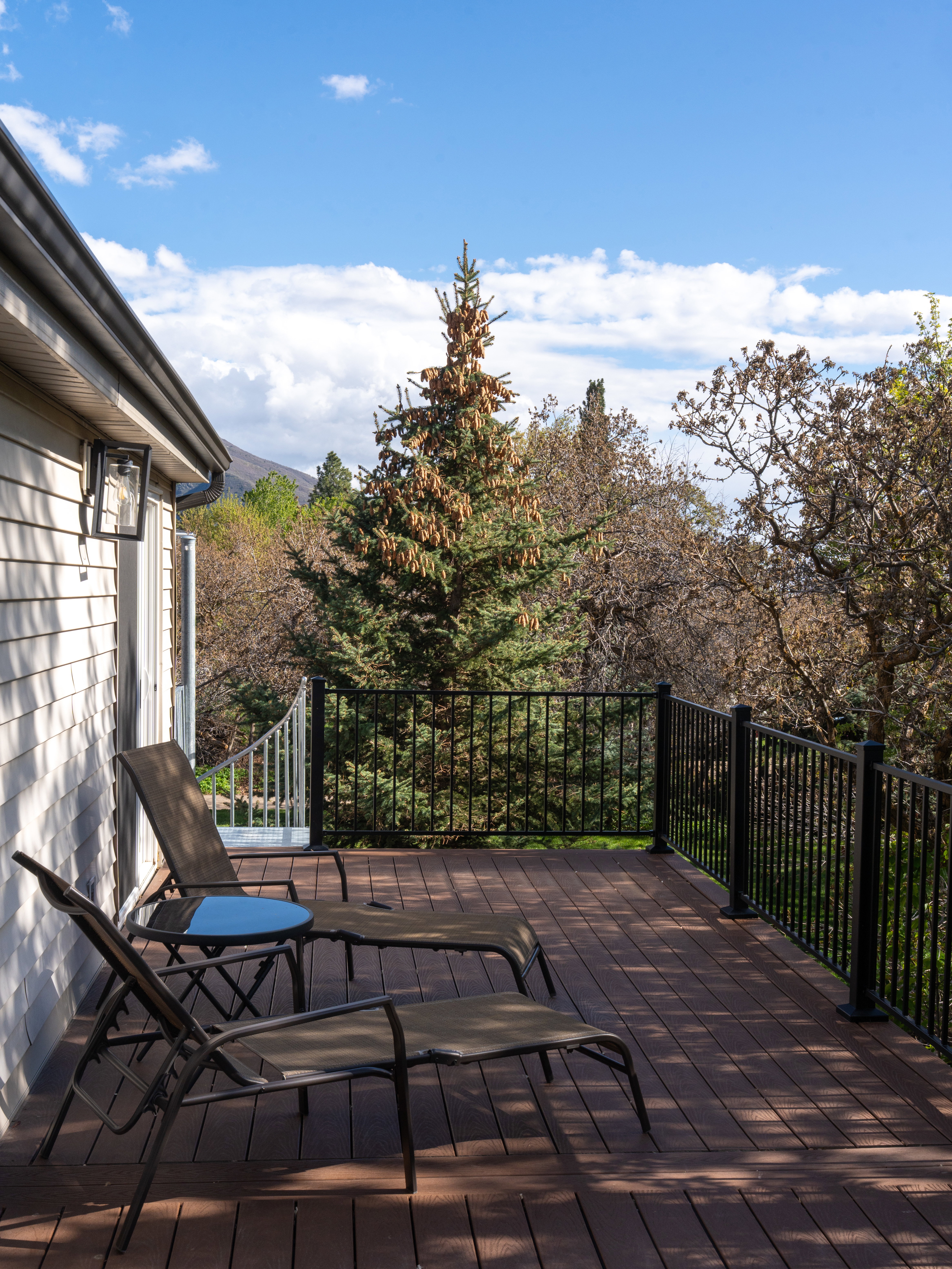 Spacious outdoor deck featuring composite wood-finish flooring, black metal railings, and exterior wall lighting