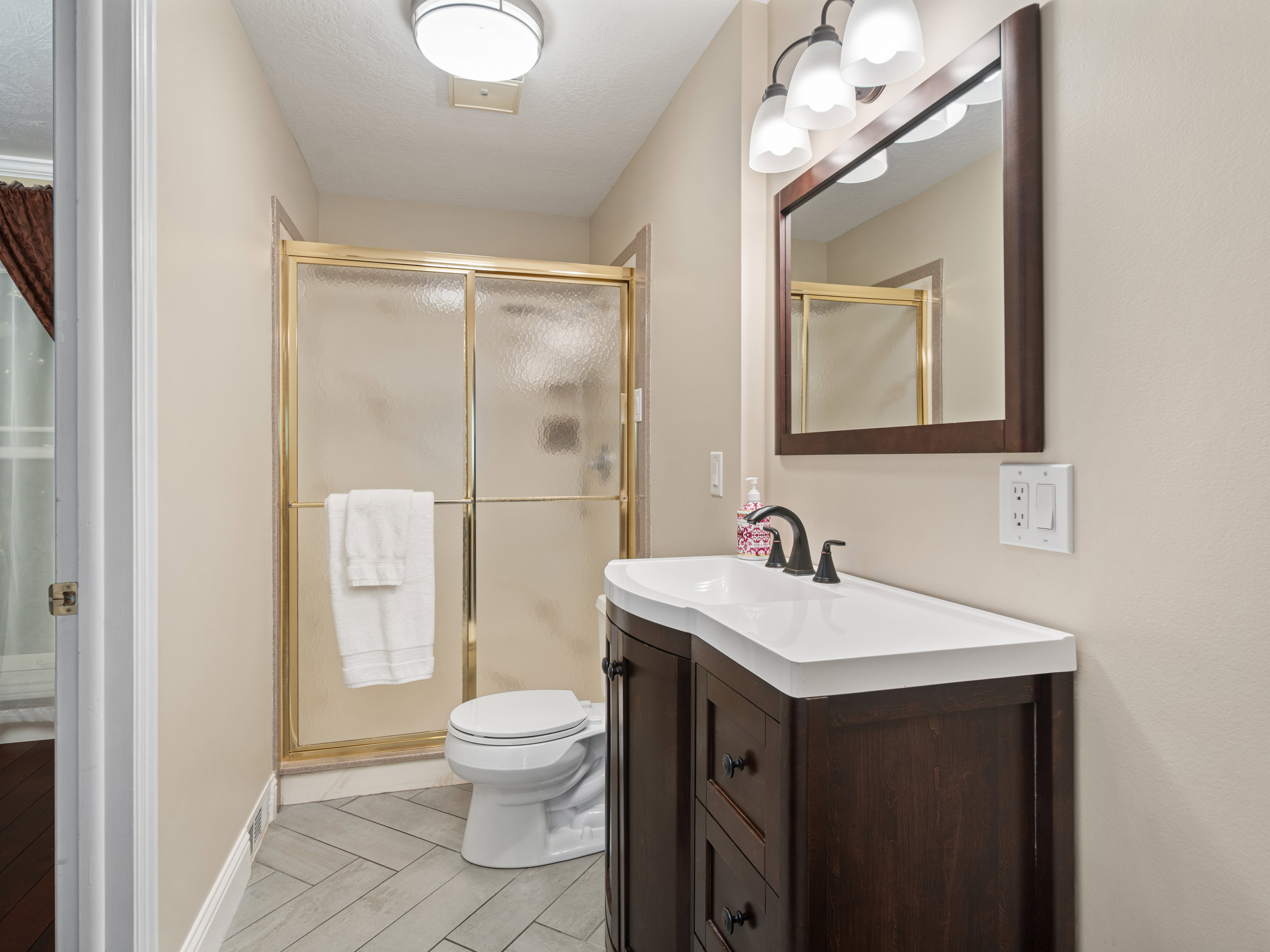 Bathroom featuring a dark wood-finish vanity with an integrated white sink, a framed mirror, and a three-light fixture