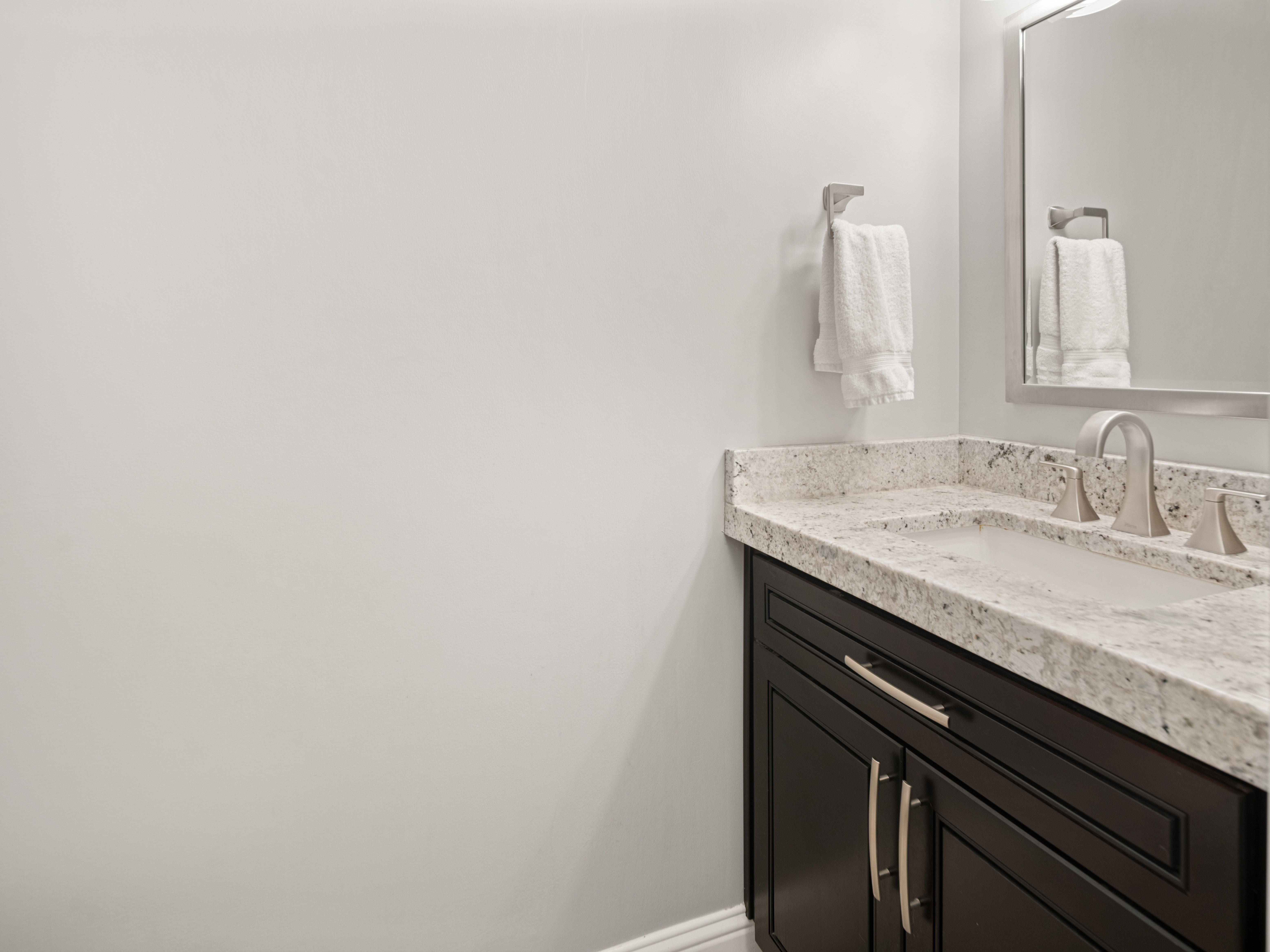 Dark wood-finish vanity with brushed nickel hardware, integrated sink, and light speckled countertop