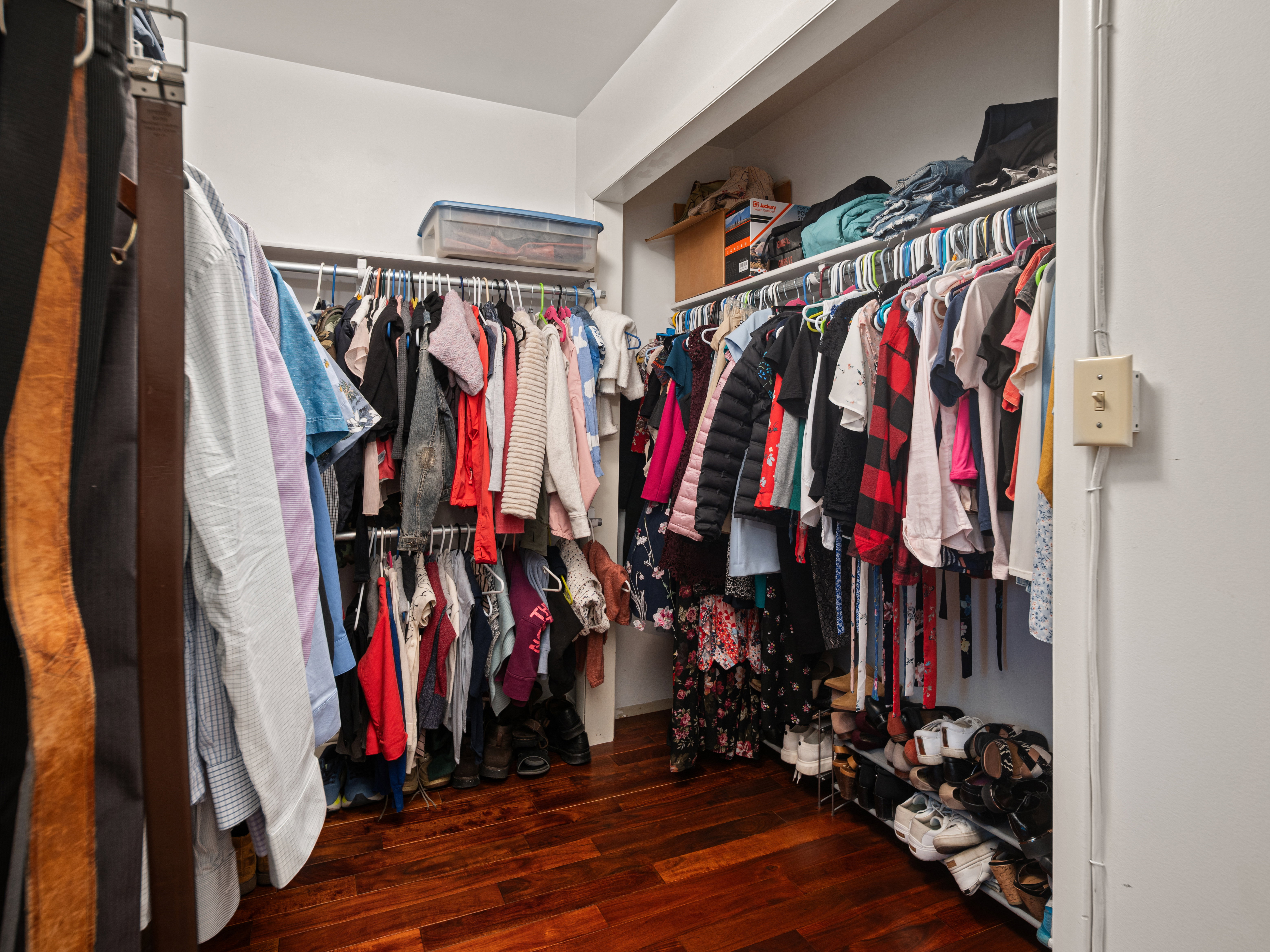 Walk-in closet featuring wood-finish flooring, ample hanging rods, and integrated shelving