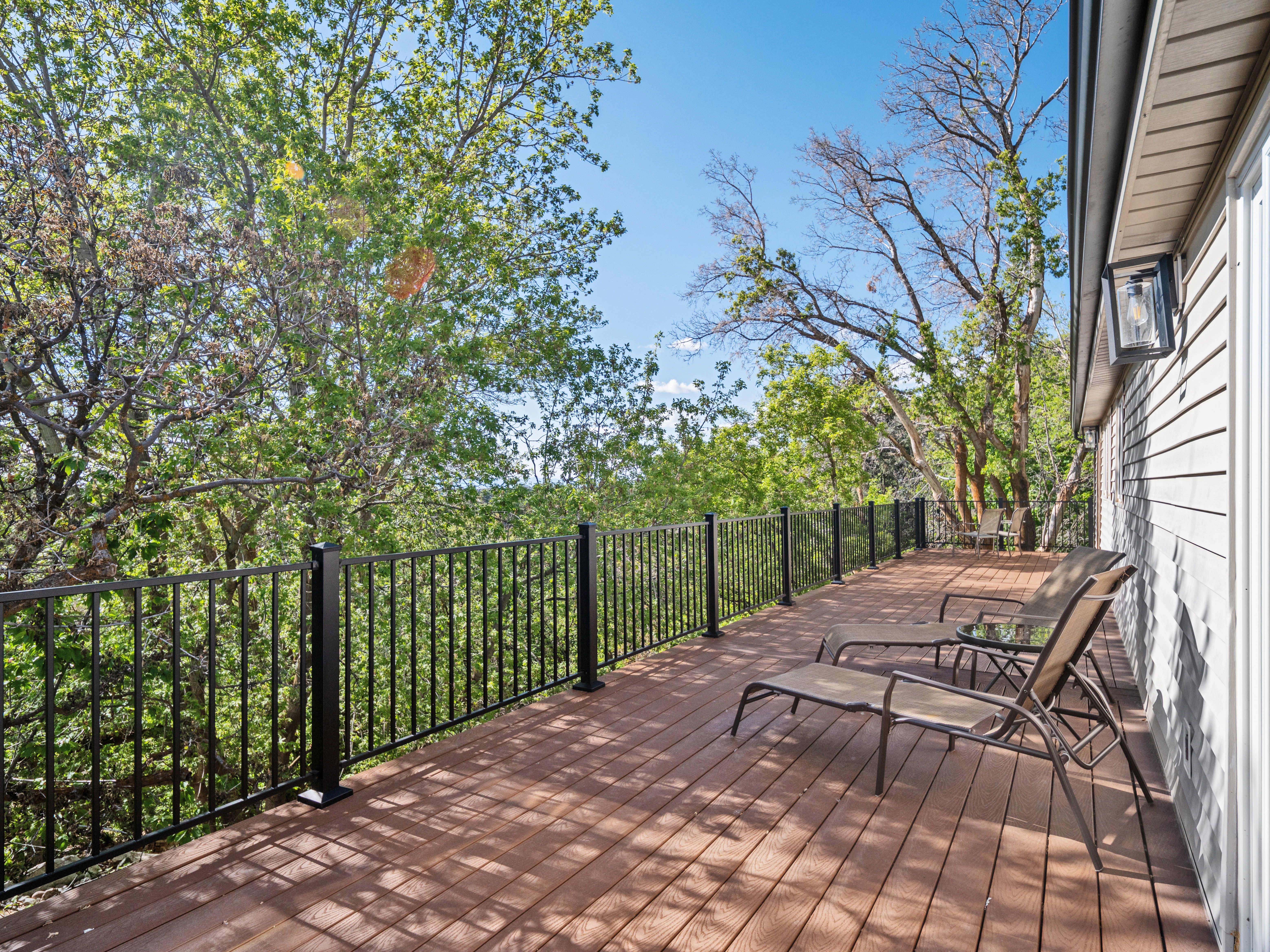 Expansive outdoor deck featuring wood-finish flooring, black metal railings, and attached exterior lighting