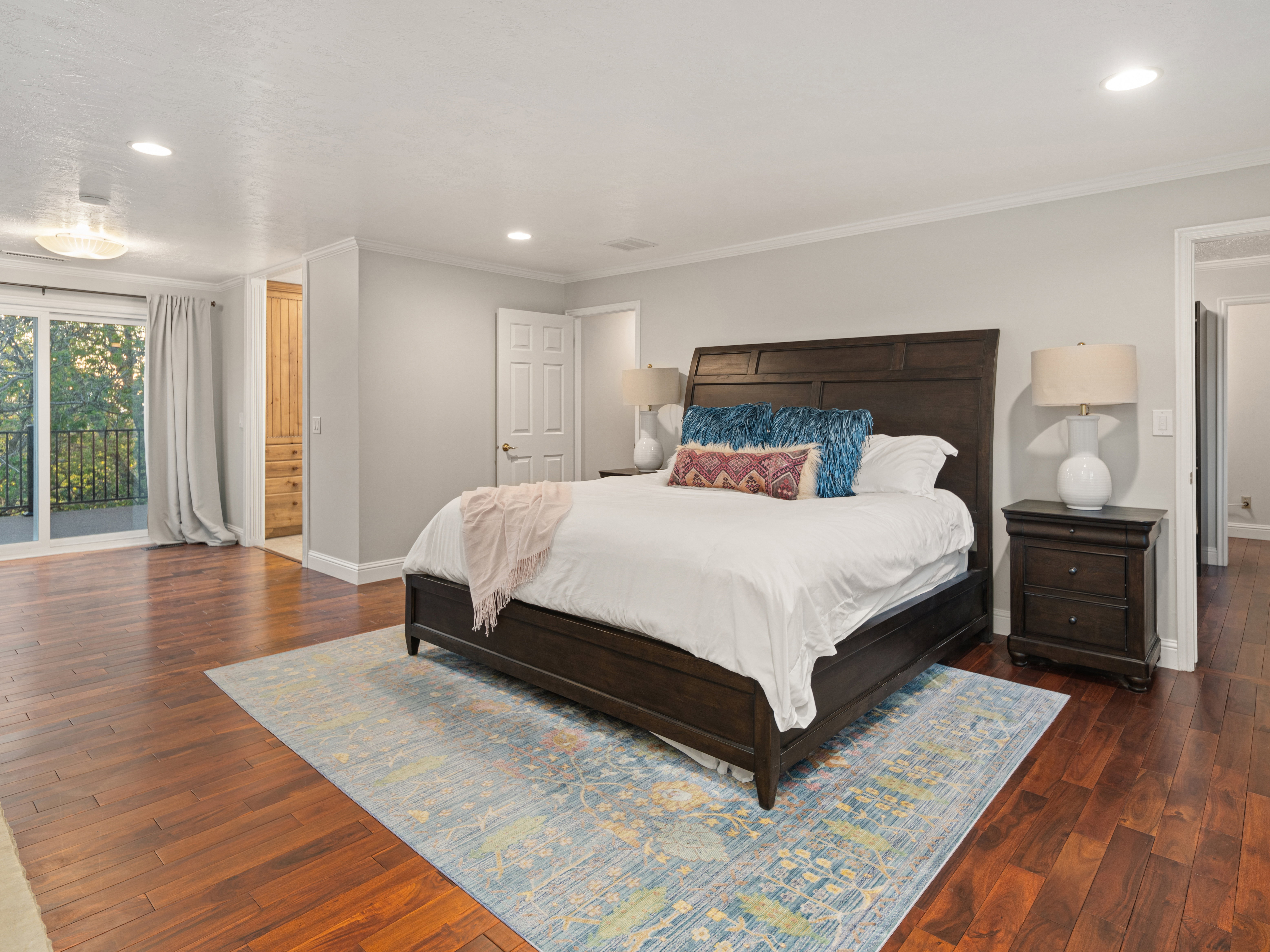 Spacious room featuring rich wood-finish flooring, recessed lighting, and a glass sliding door opening to a balcony with black railings