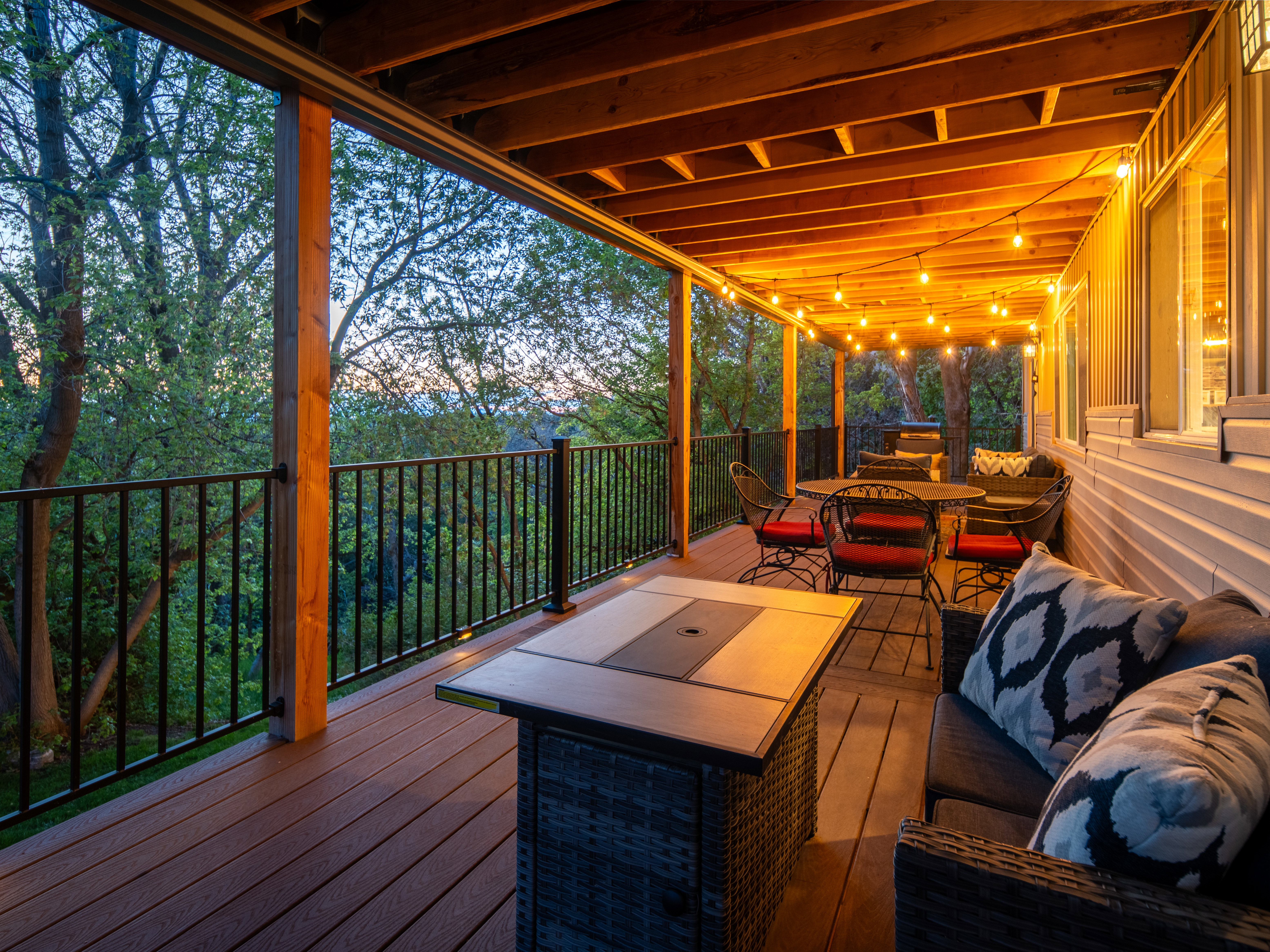 Expansive covered deck featuring composite decking, exposed wood beam ceiling, string lighting, and black metal railings