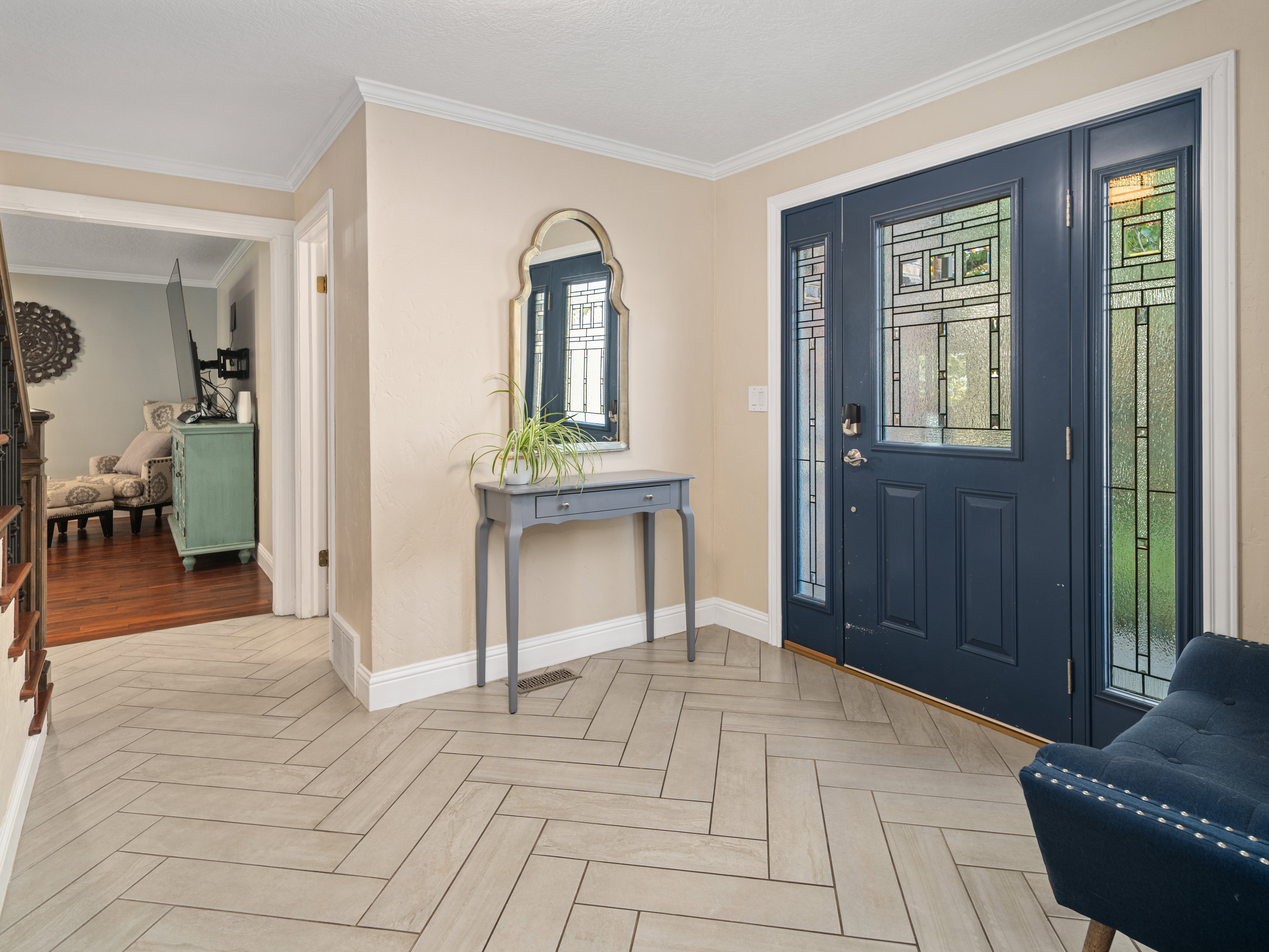 Entryway featuring a dark blue door with decorative glass inserts and sidelights, herringbone-patterned tile flooring, and white baseboards