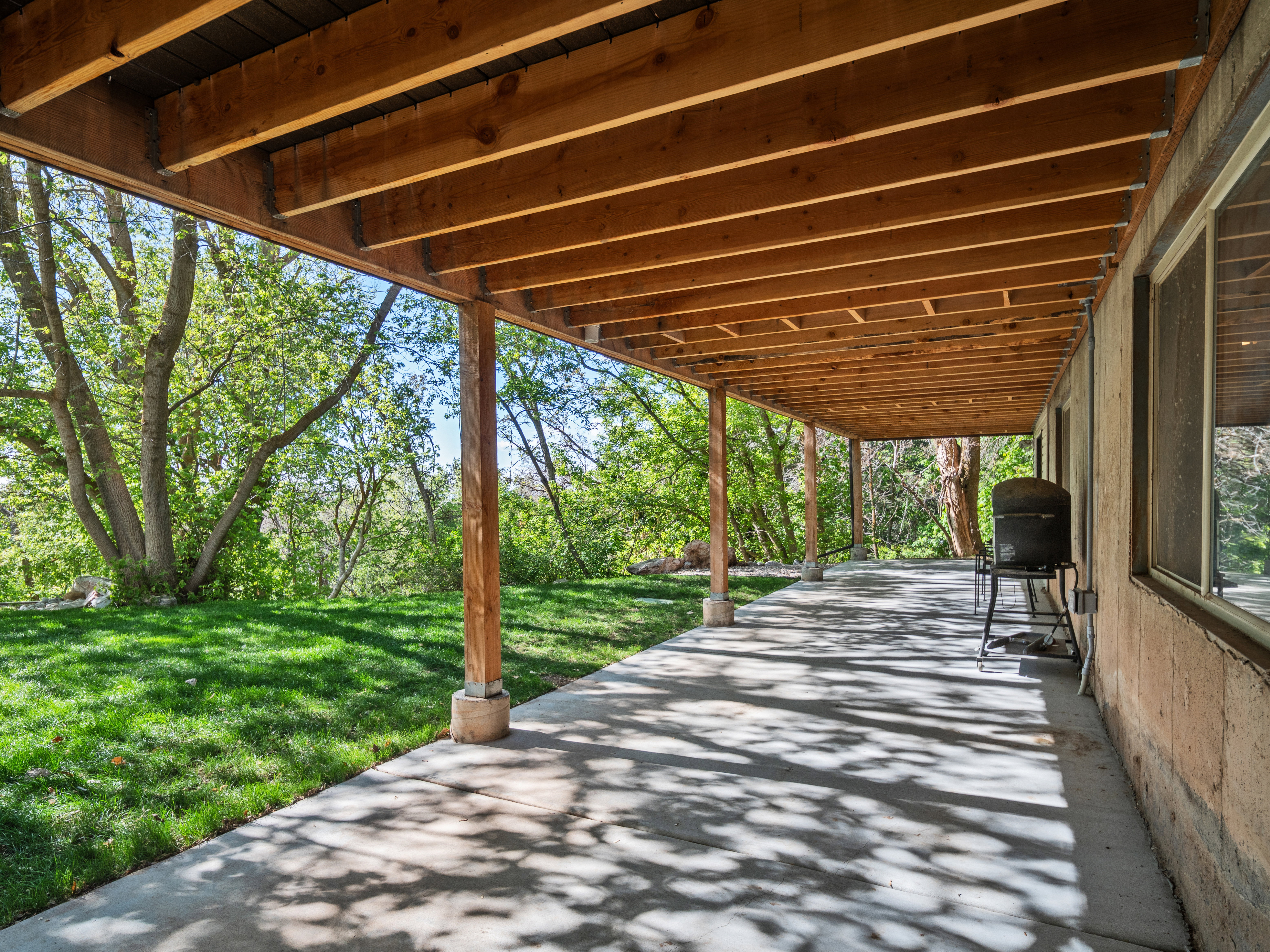 Covered patio with a concrete surface, supported by wooden beams and posts