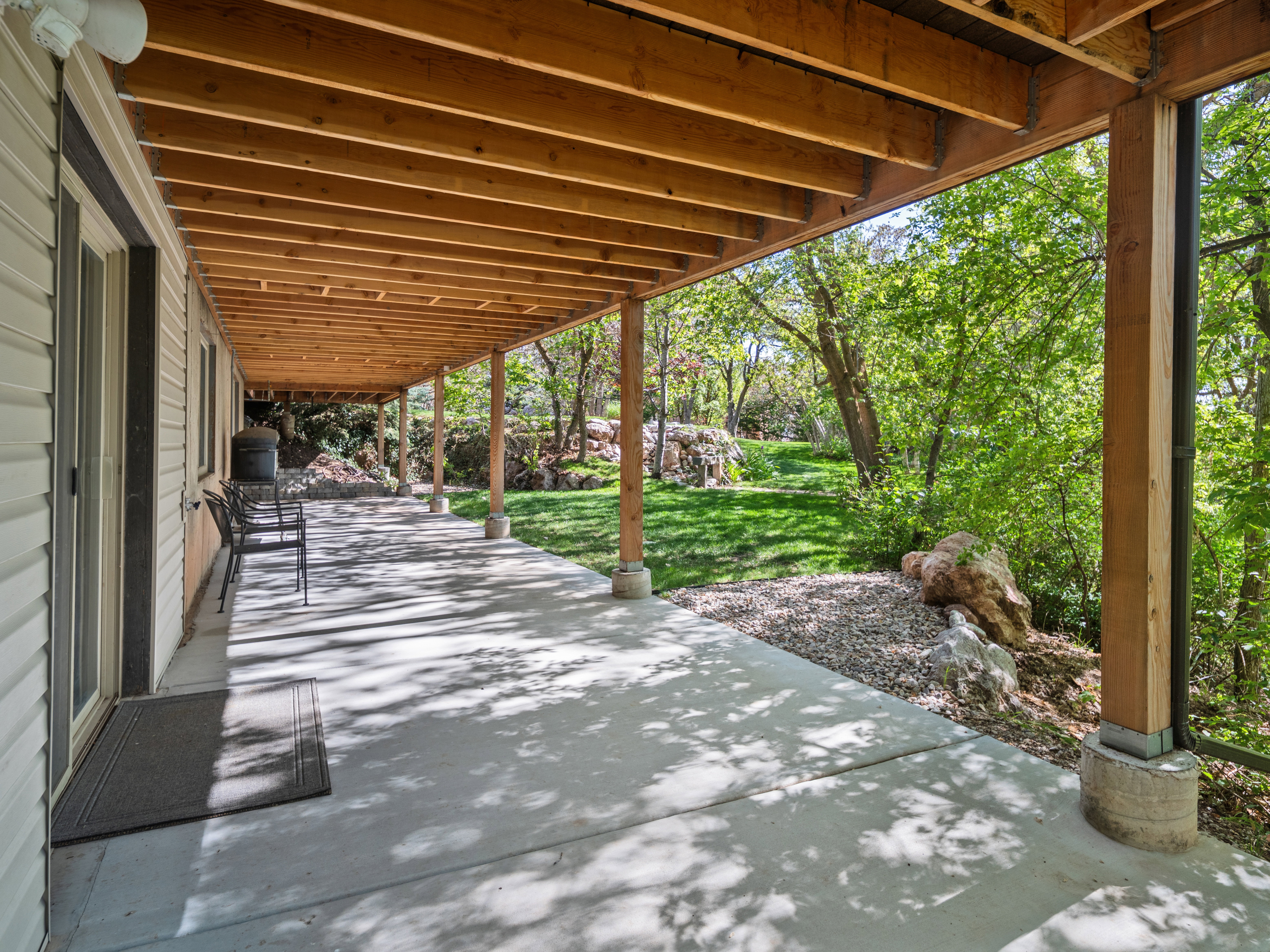 Expansive covered patio featuring a concrete surface, exposed wood beam ceiling, and timber support columns