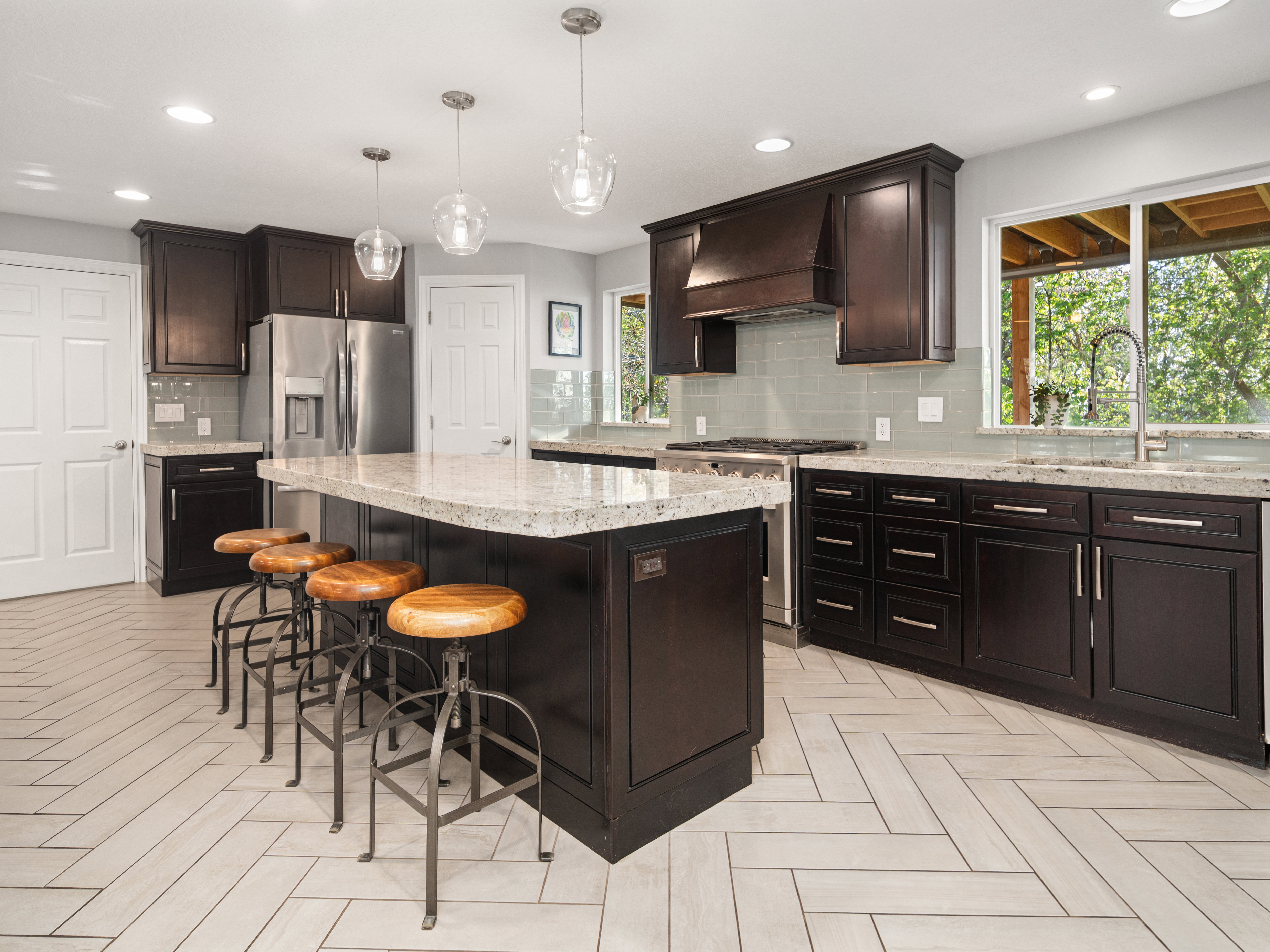 Spacious kitchen featuring an island with pendant lighting, dark wood cabinetry, light-toned countertops, and a full-height tile backsplash