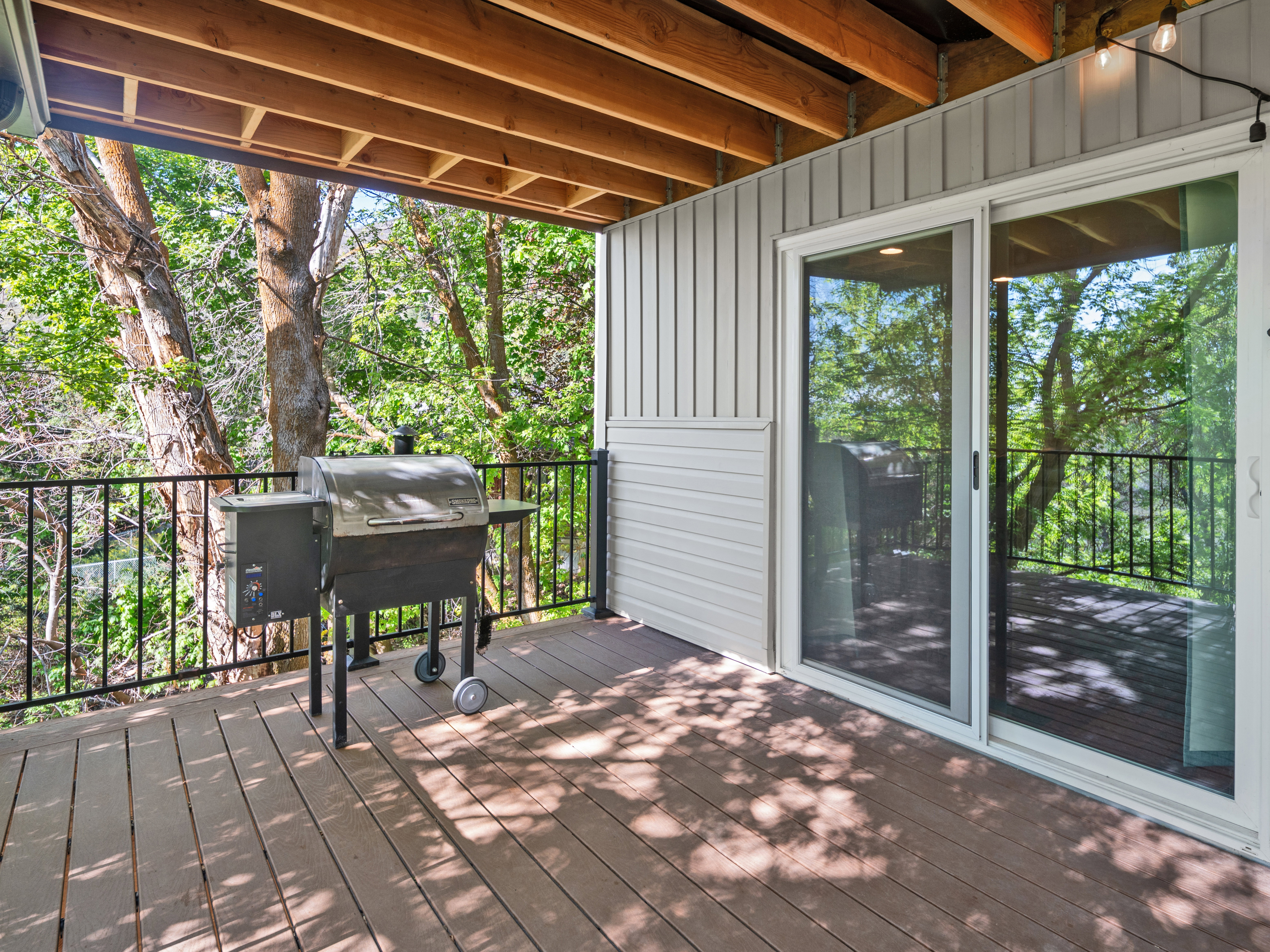 Expansive outdoor deck featuring wood-finish flooring, black metal railings, and a sliding glass door entry
