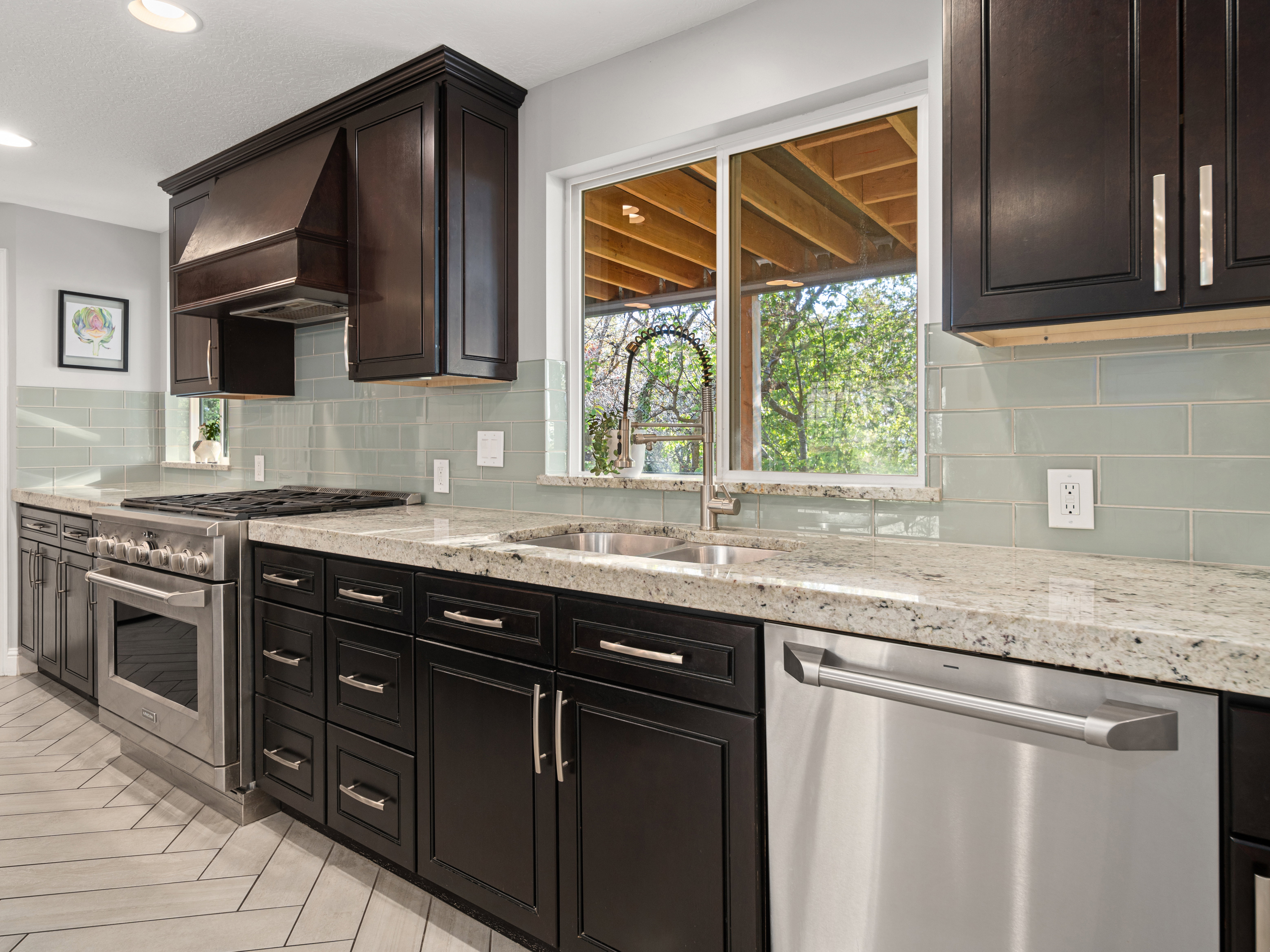 Kitchen featuring dark wood cabinetry with stainless steel hardware, light-toned stone countertops, and a subway tile backsplash