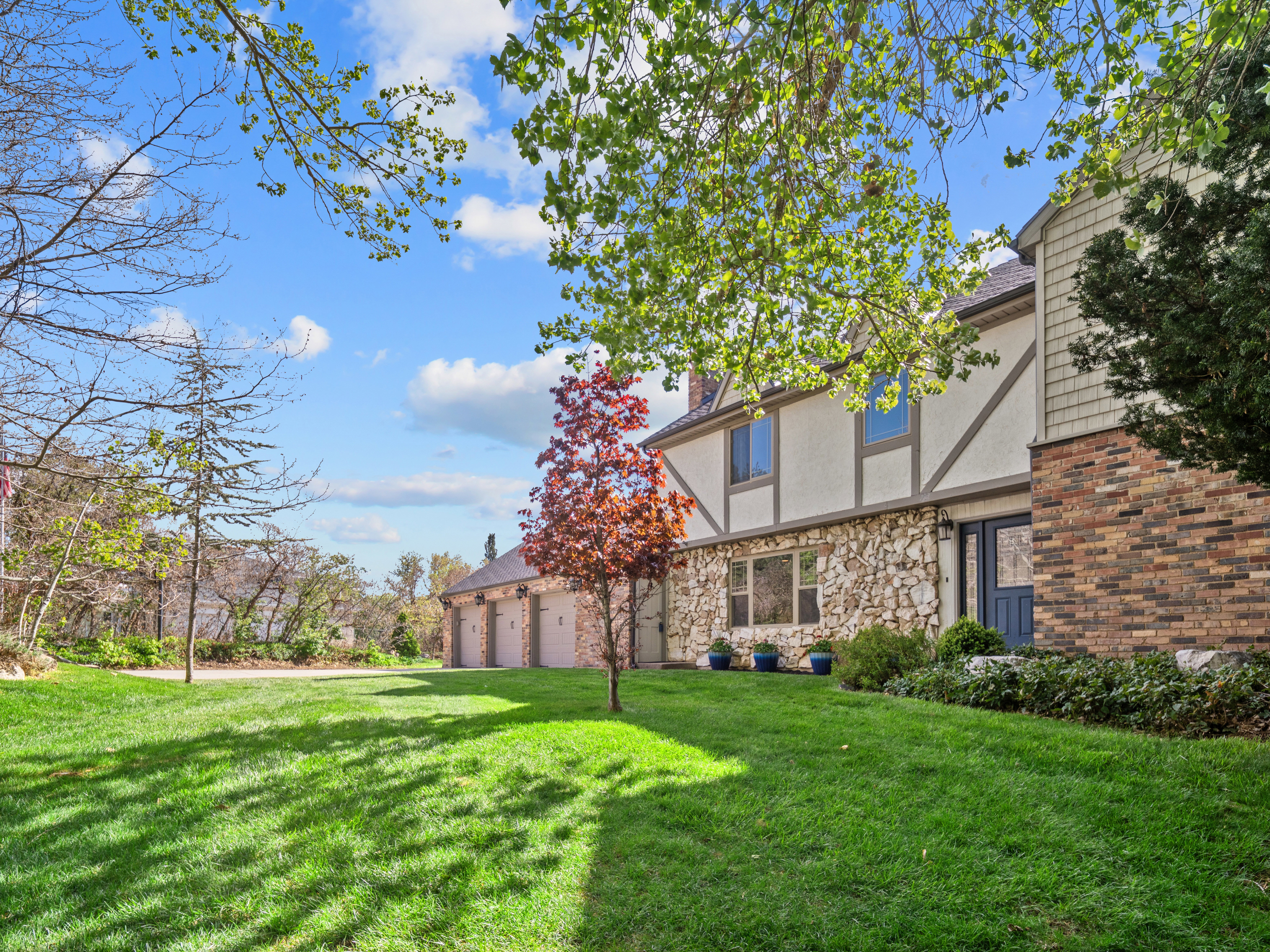 Exterior featuring stone and stucco finishes with timber accents, a multi-car garage, and a lush green lawn