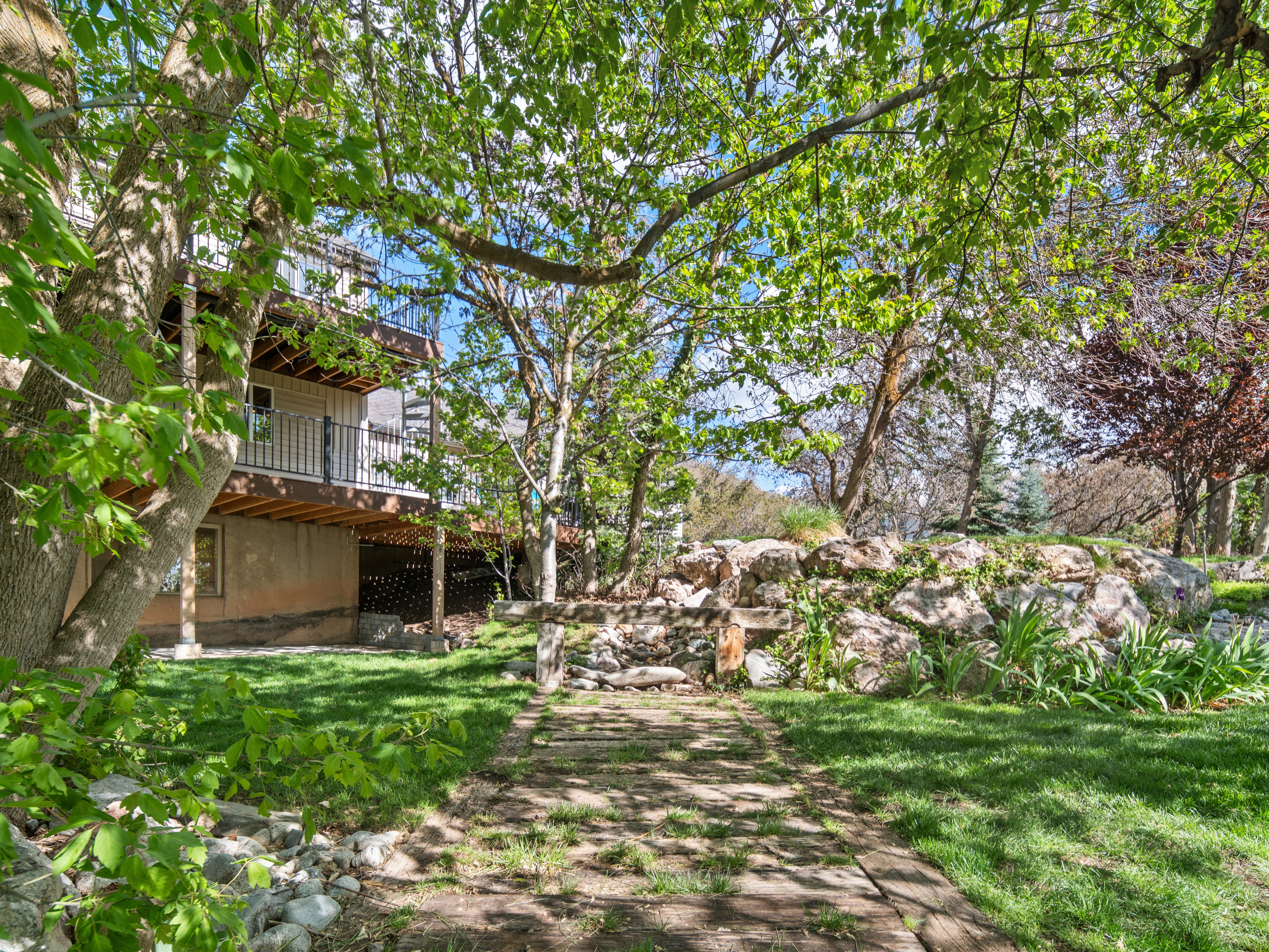 Tiered backyard featuring a decorative rock wall, established trees, and a wooden walkway