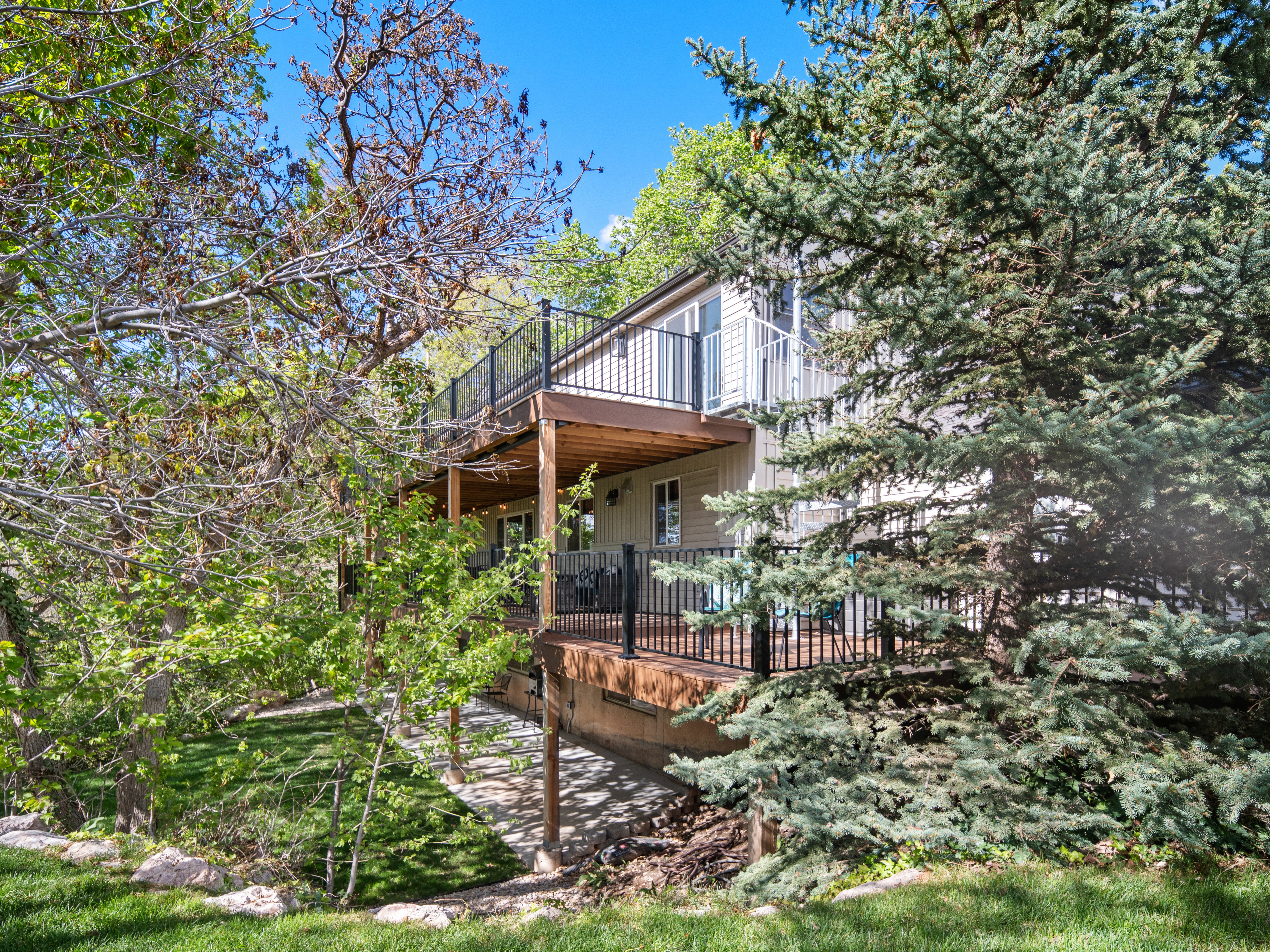 Multi-level deck with black metal railings, surrounded by mature trees and lush green landscaping