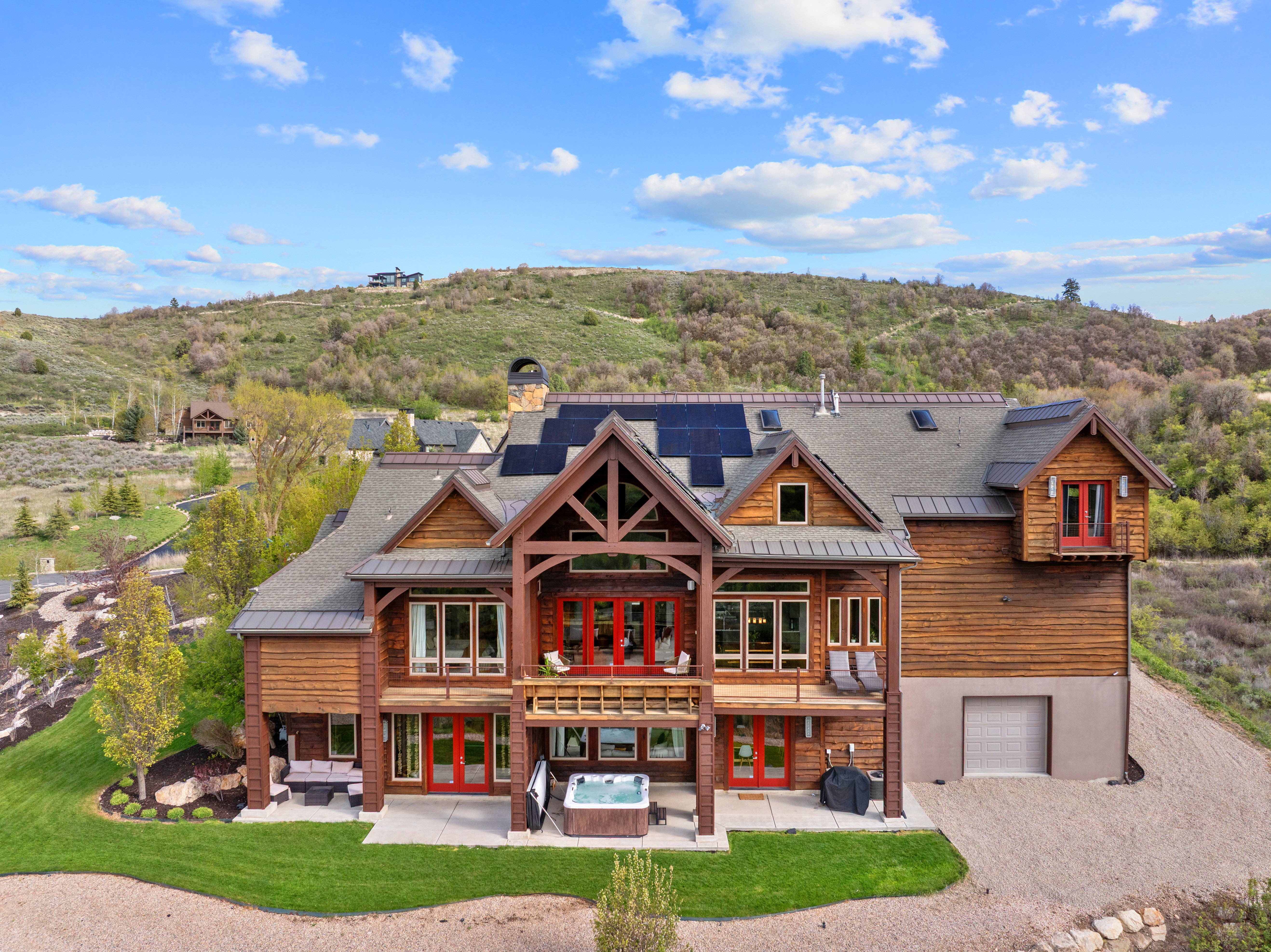 Timber-frame exterior featuring multiple balconies, a lower-level patio with an attached hot tub, and an integrated garage