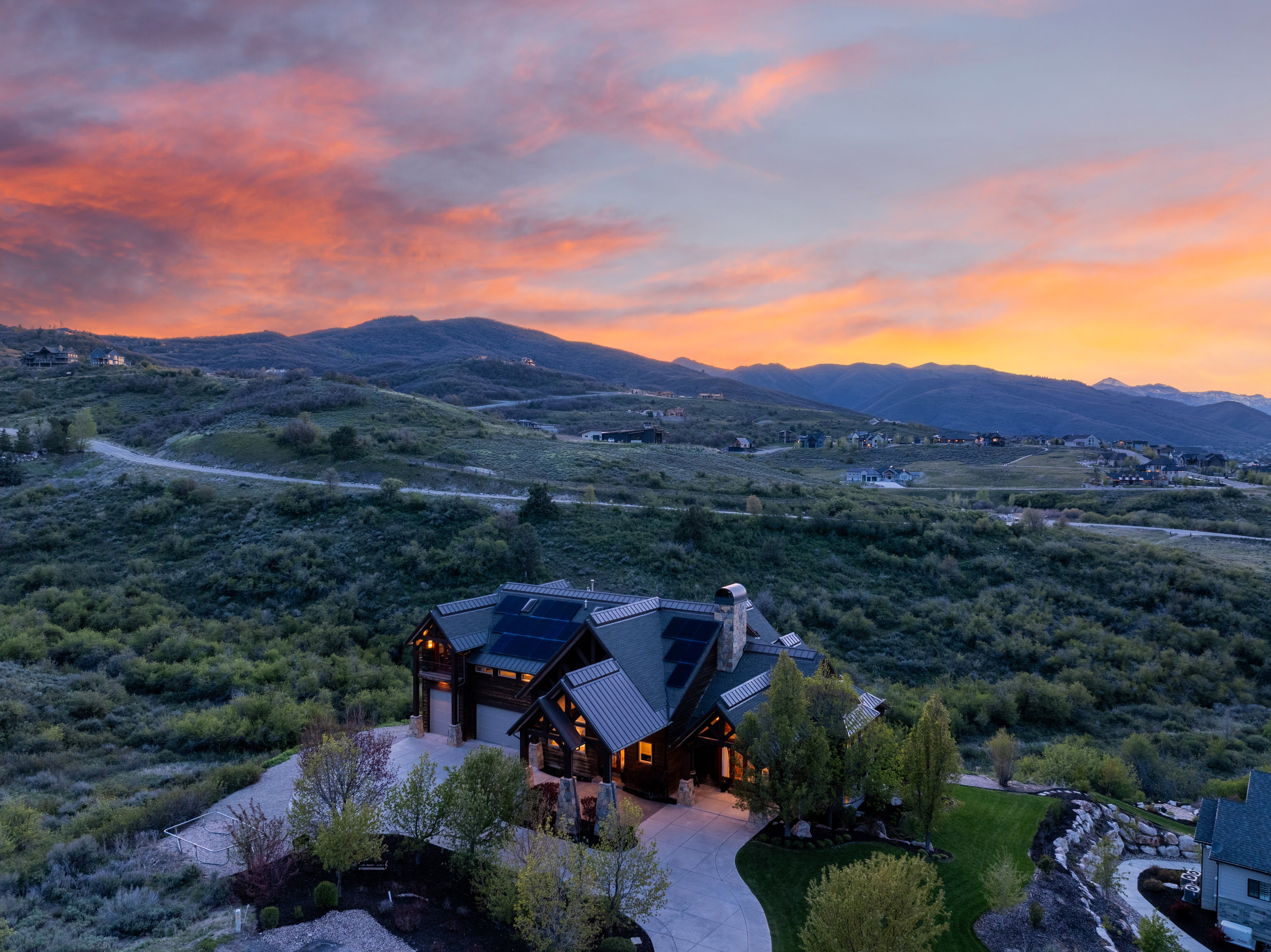 Mountain-style residence featuring a dark-toned roof, multiple solar panels, and a prominent stone chimney