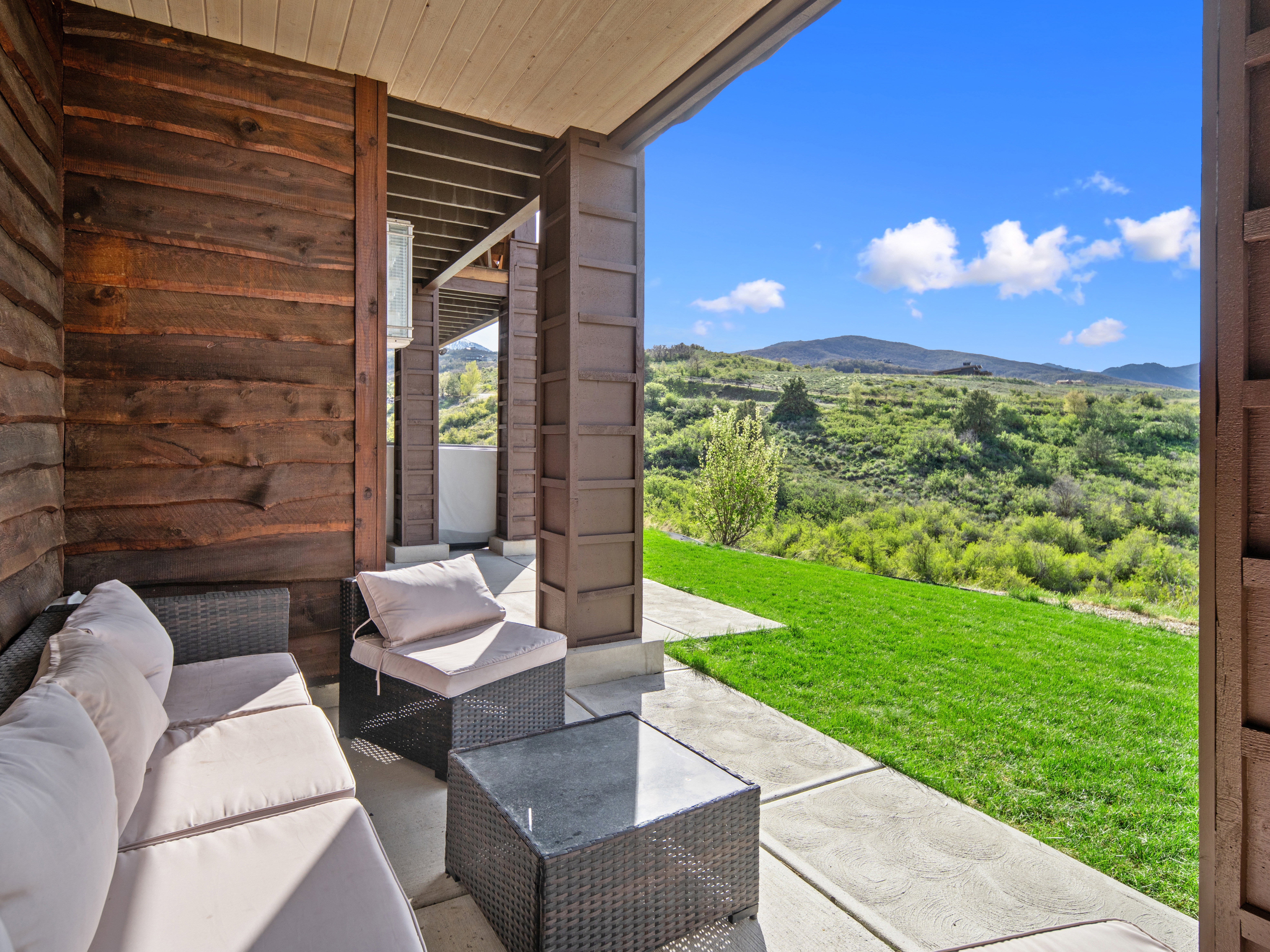 Covered patio with a concrete surface and rich wood-paneled wall, overlooking a manicured lawn and distant hills