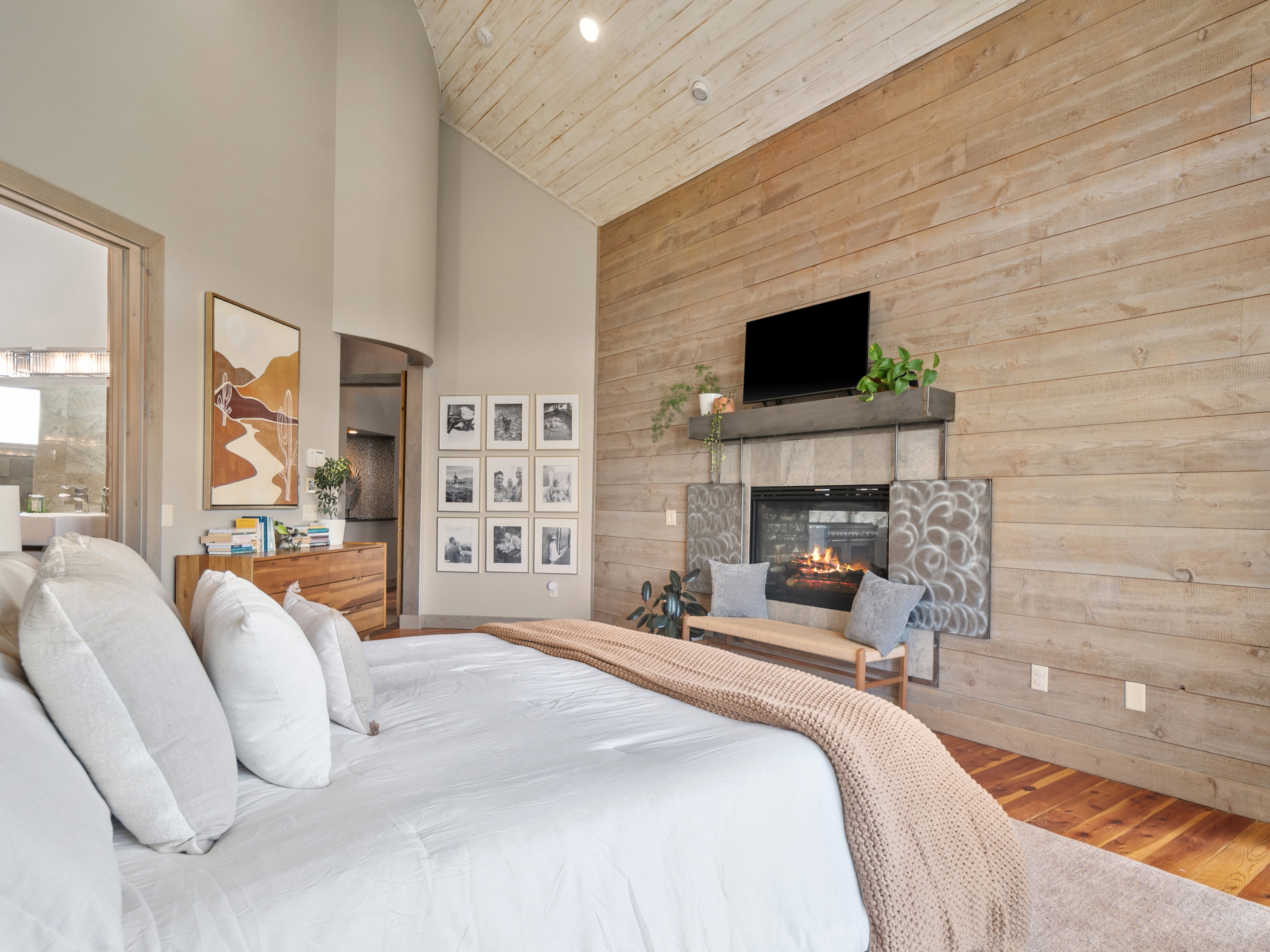 Vaulted wood-plank ceiling, wood-finish accent wall, and a built-in fireplace with a stone surround