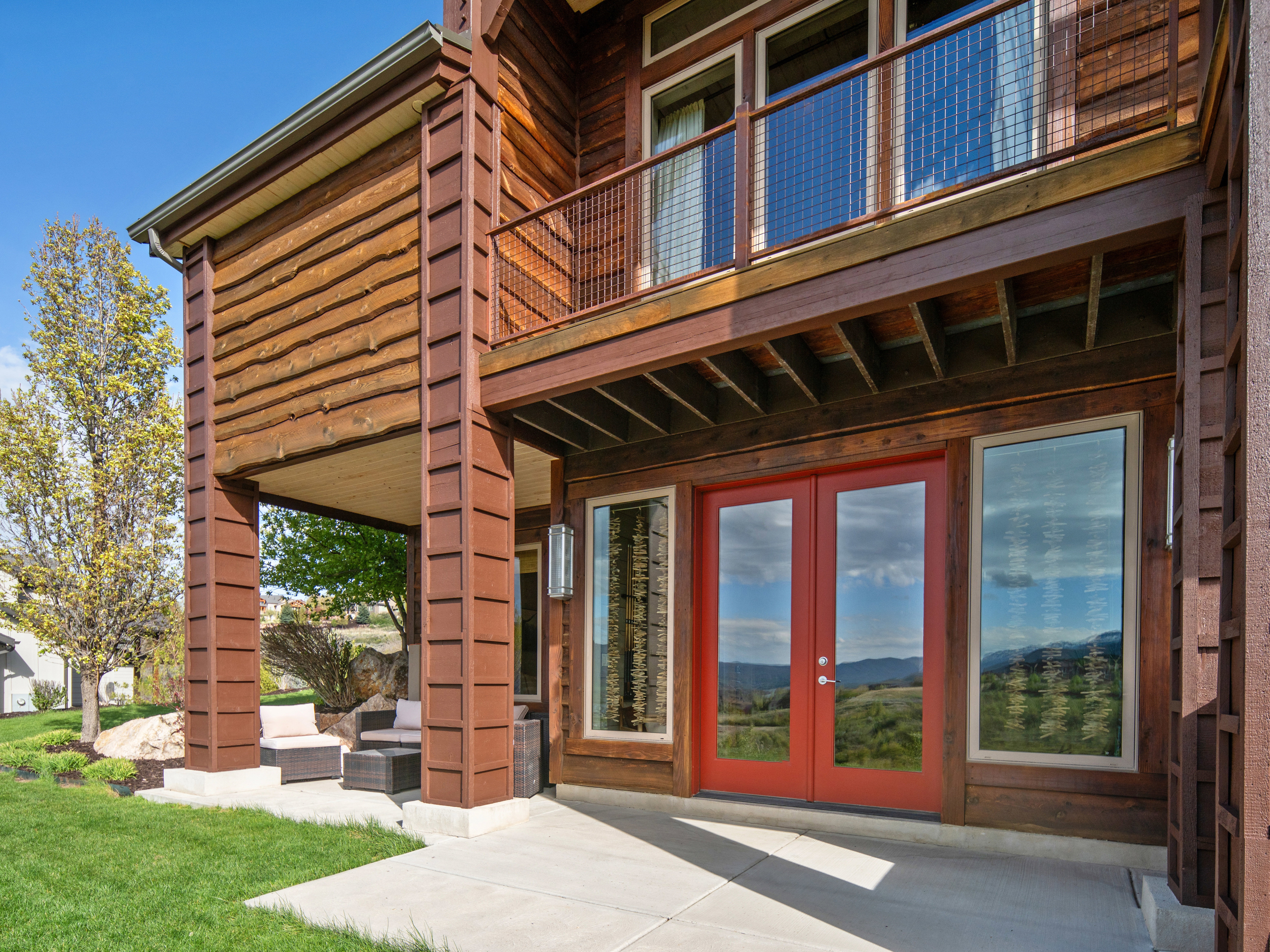 Exterior featuring wood siding, a second-story balcony with metal mesh railing, and a ground-level patio