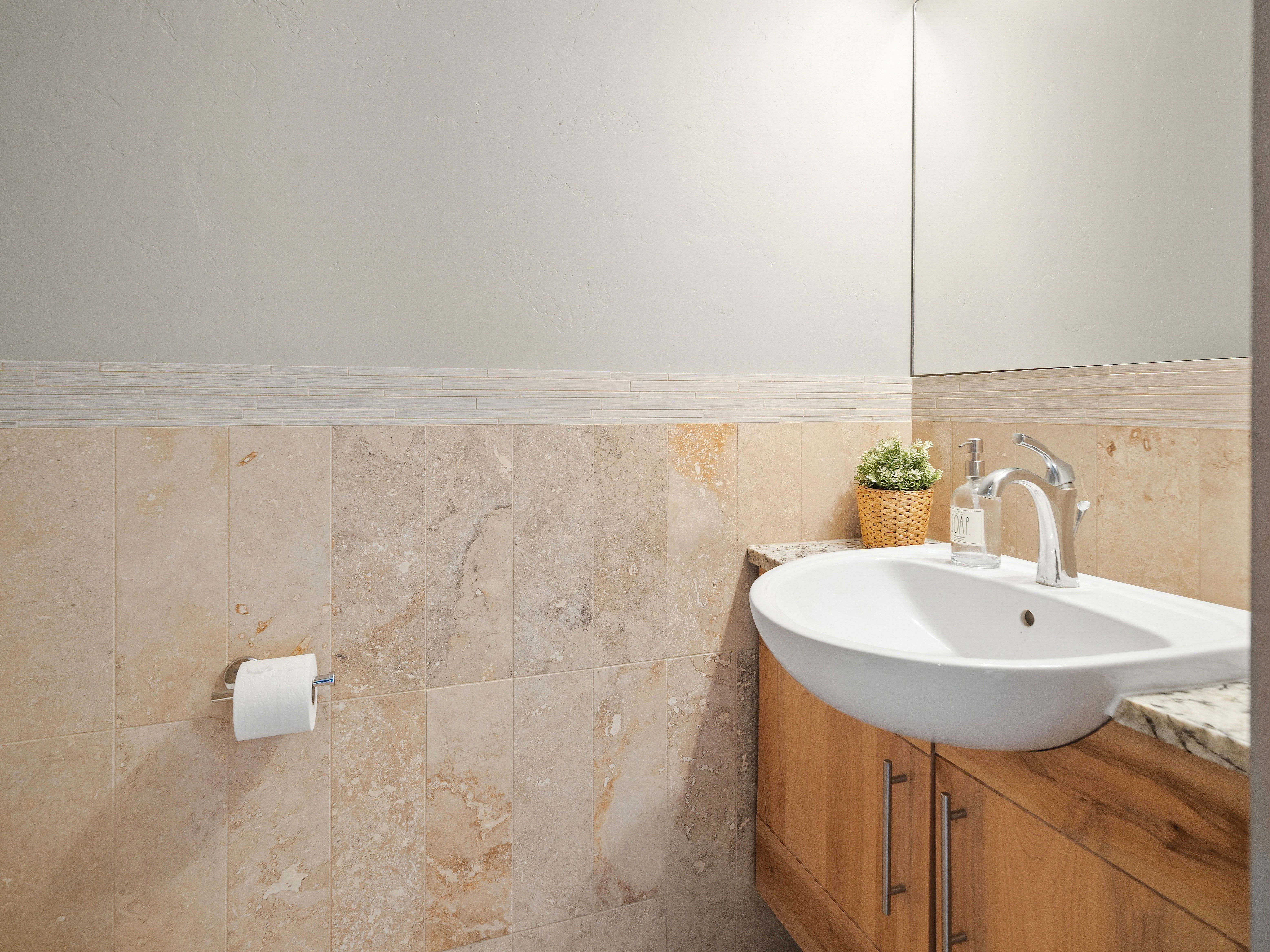 Powder room featuring natural stone tile wainscoting with a decorative glass tile accent strip, a light wood-finish vanity with a granite countertop, a contemporary vessel sink, and a sleek chrome faucet