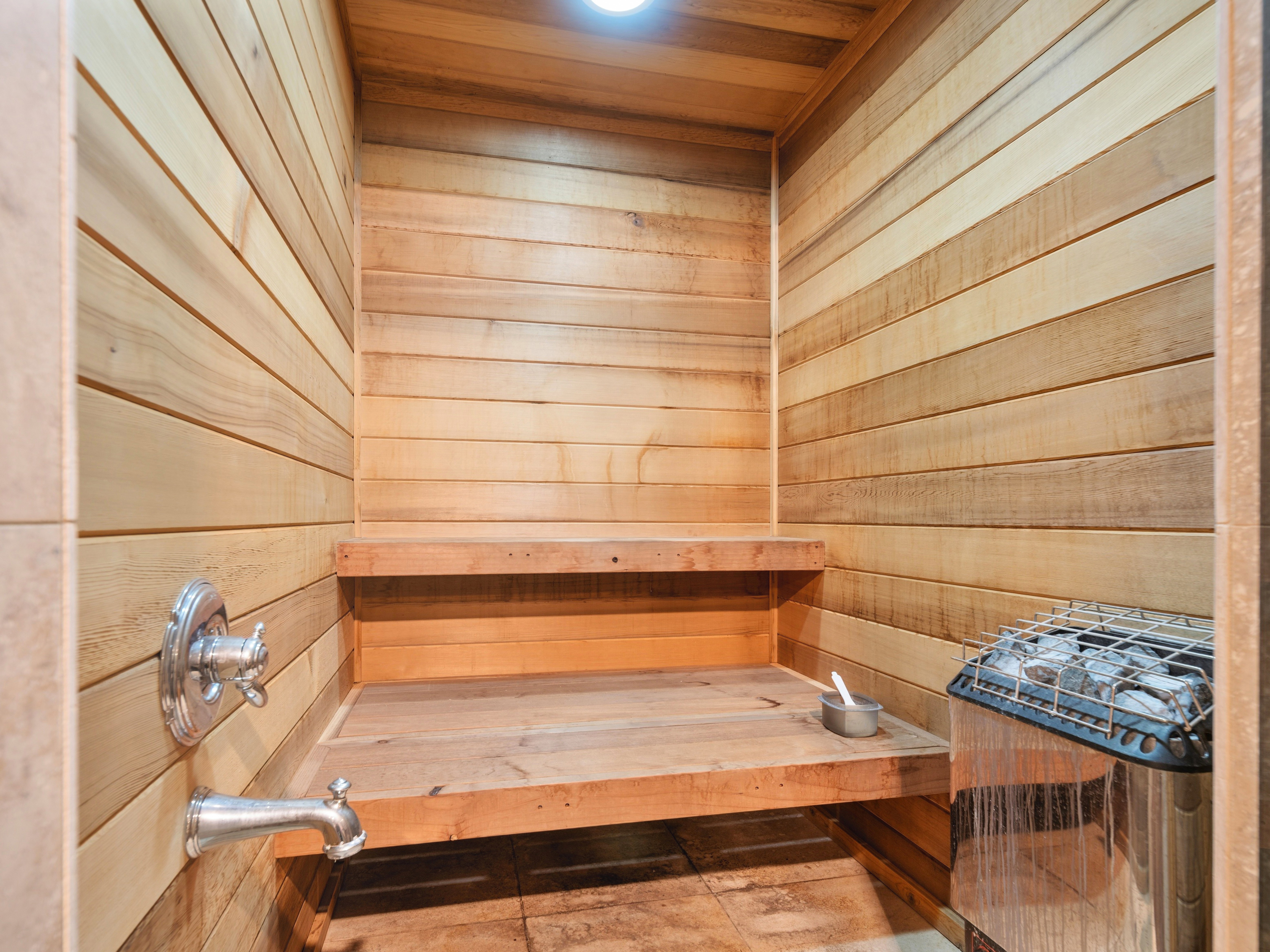 Sauna featuring light wood plank walls, two-tiered wood benches, and a built-in sauna heater