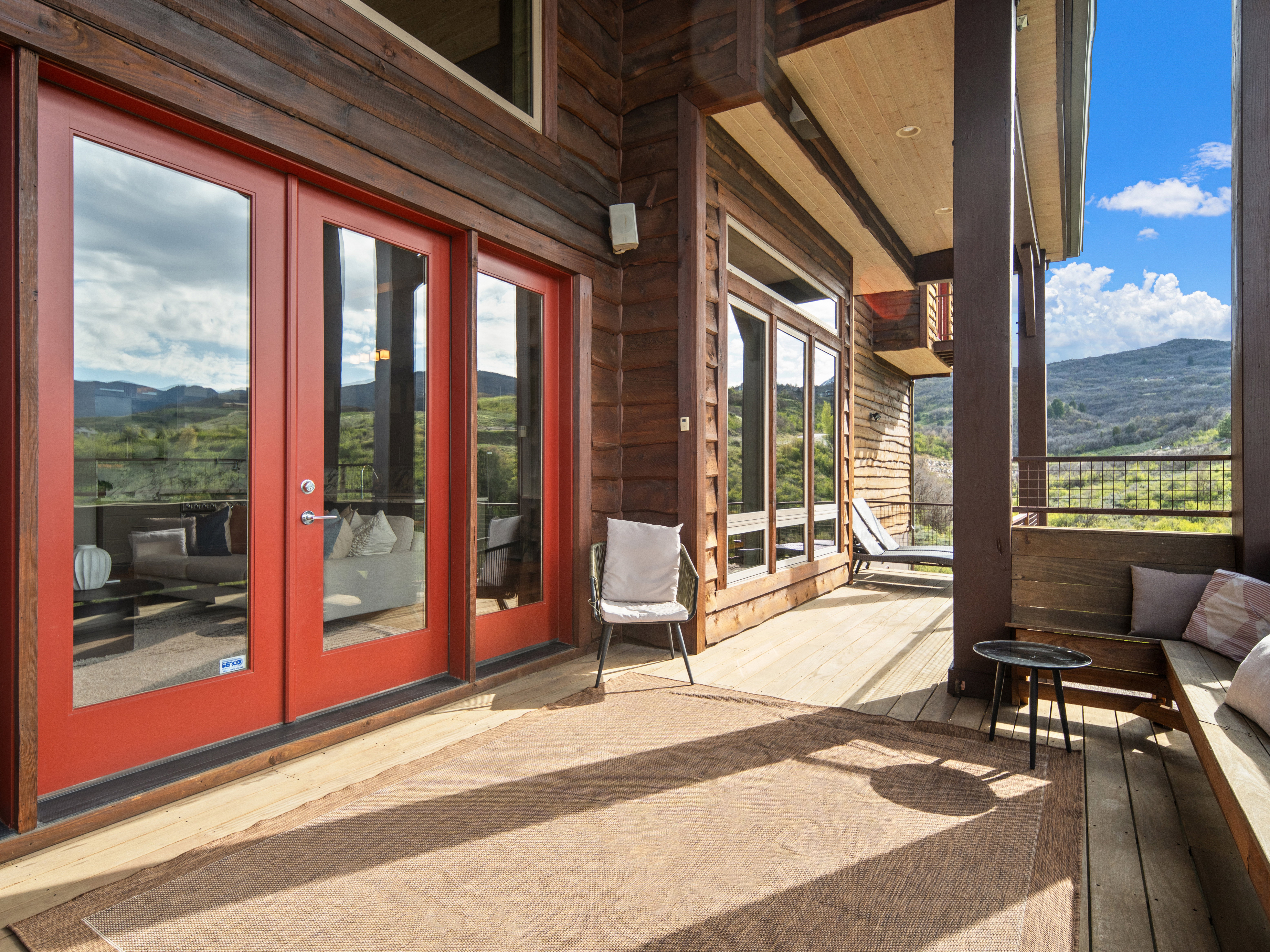 Expansive wood-finish deck with red French doors, full-height windows, a wooden built-in bench, and a mountain backdrop
