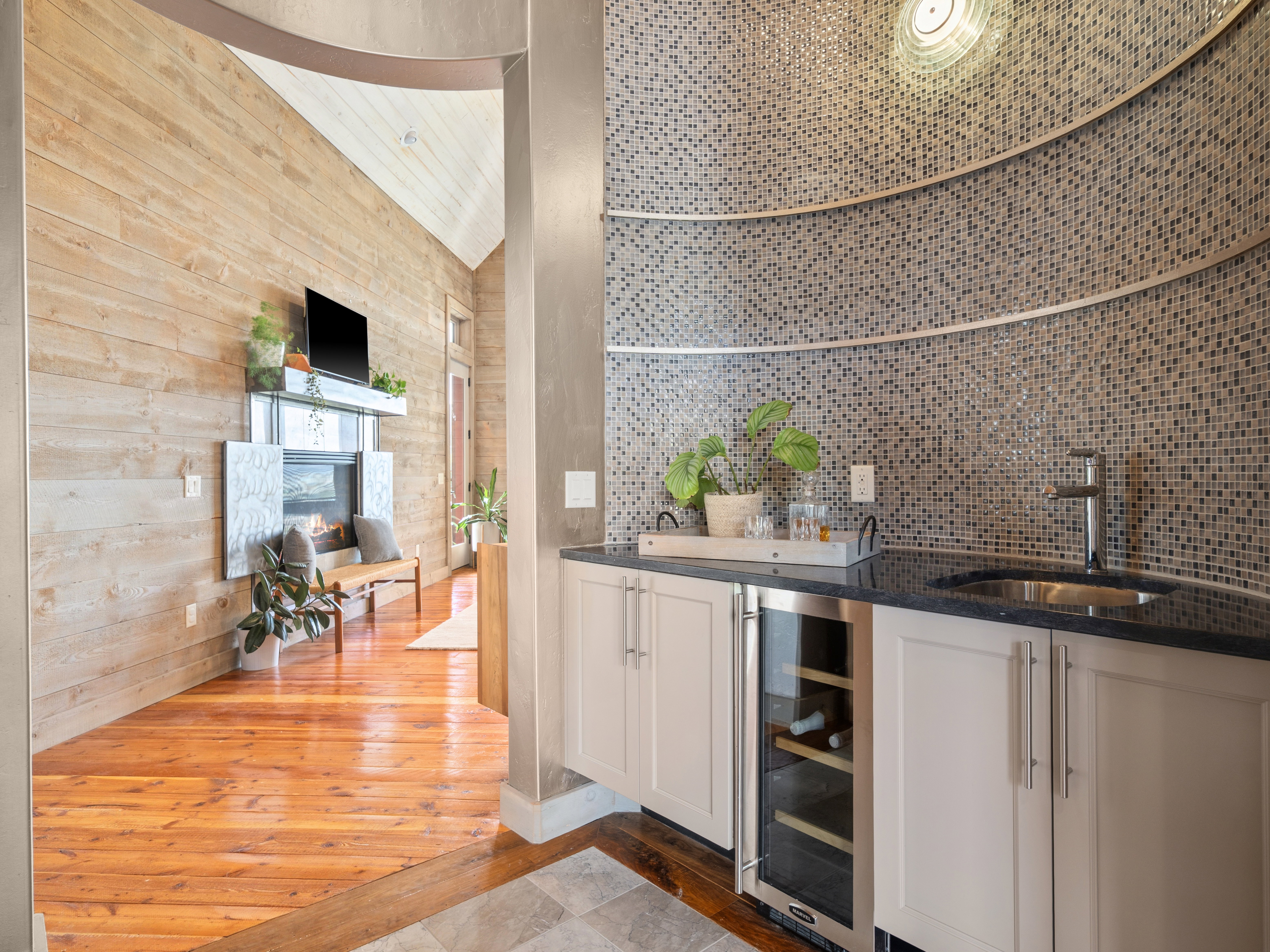 Custom wet bar with mosaic tile wall, integrated wine refrigerator, and dark countertop