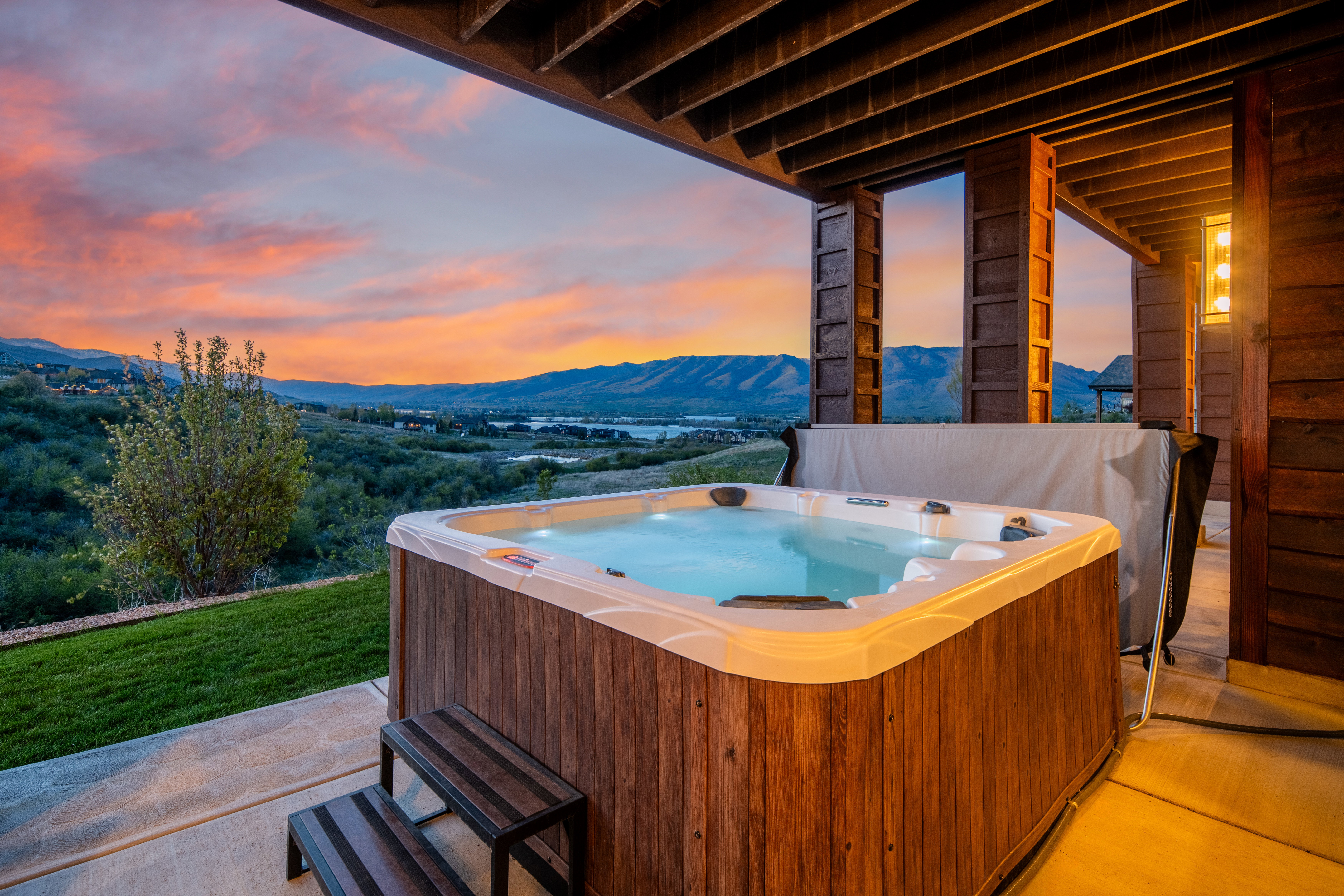 Covered patio featuring an illuminated hot tub with wood-finish siding, a concrete surface, and a built-in step stool