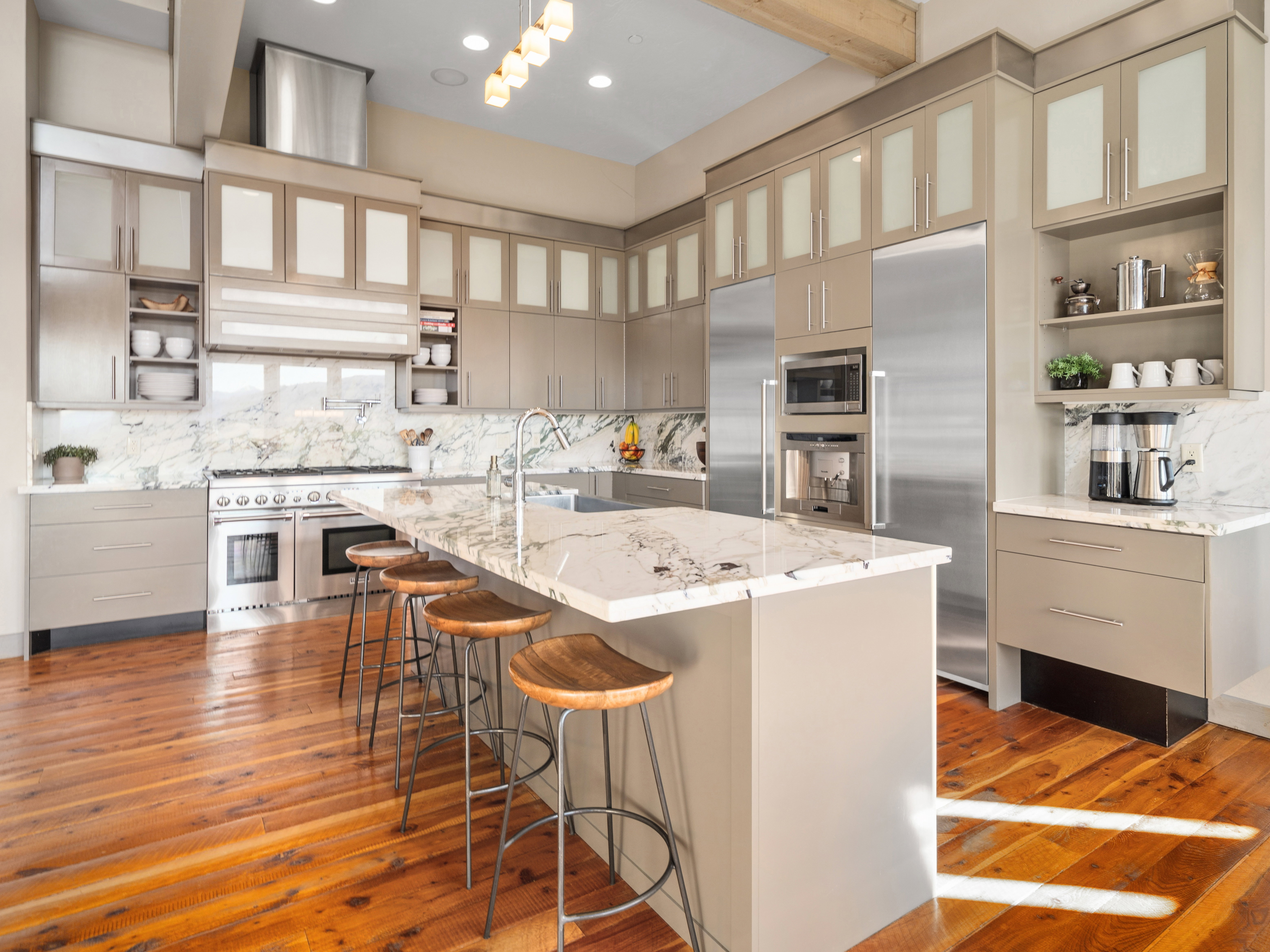Gourmet kitchen featuring a large central island with a waterfall countertop, stainless steel appliances, extensive cabinetry, light wood-finish flooring, and a stone backsplash