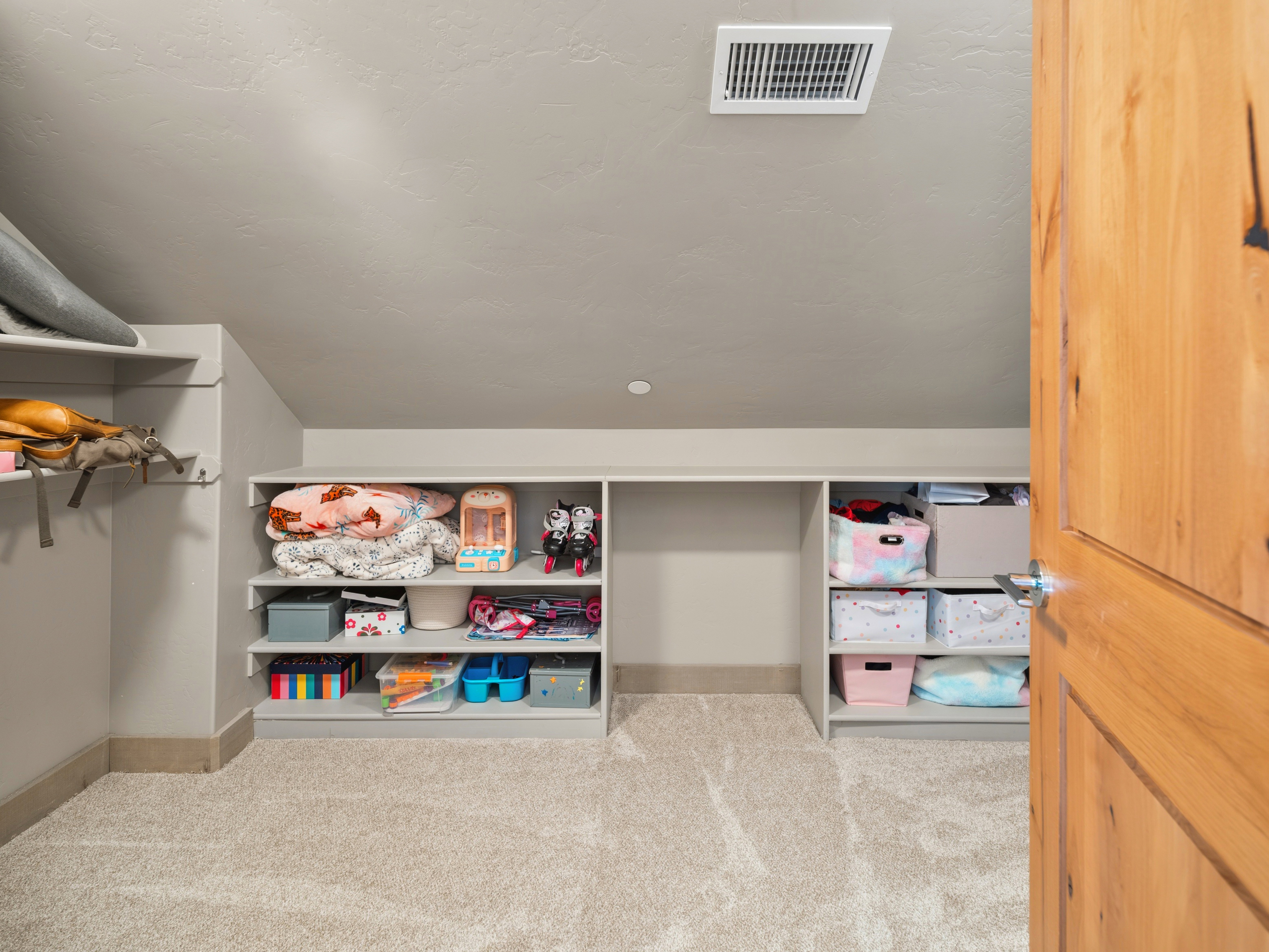 Carpeted attic space featuring built-in shelving units, sloped ceilings, and a natural wood door