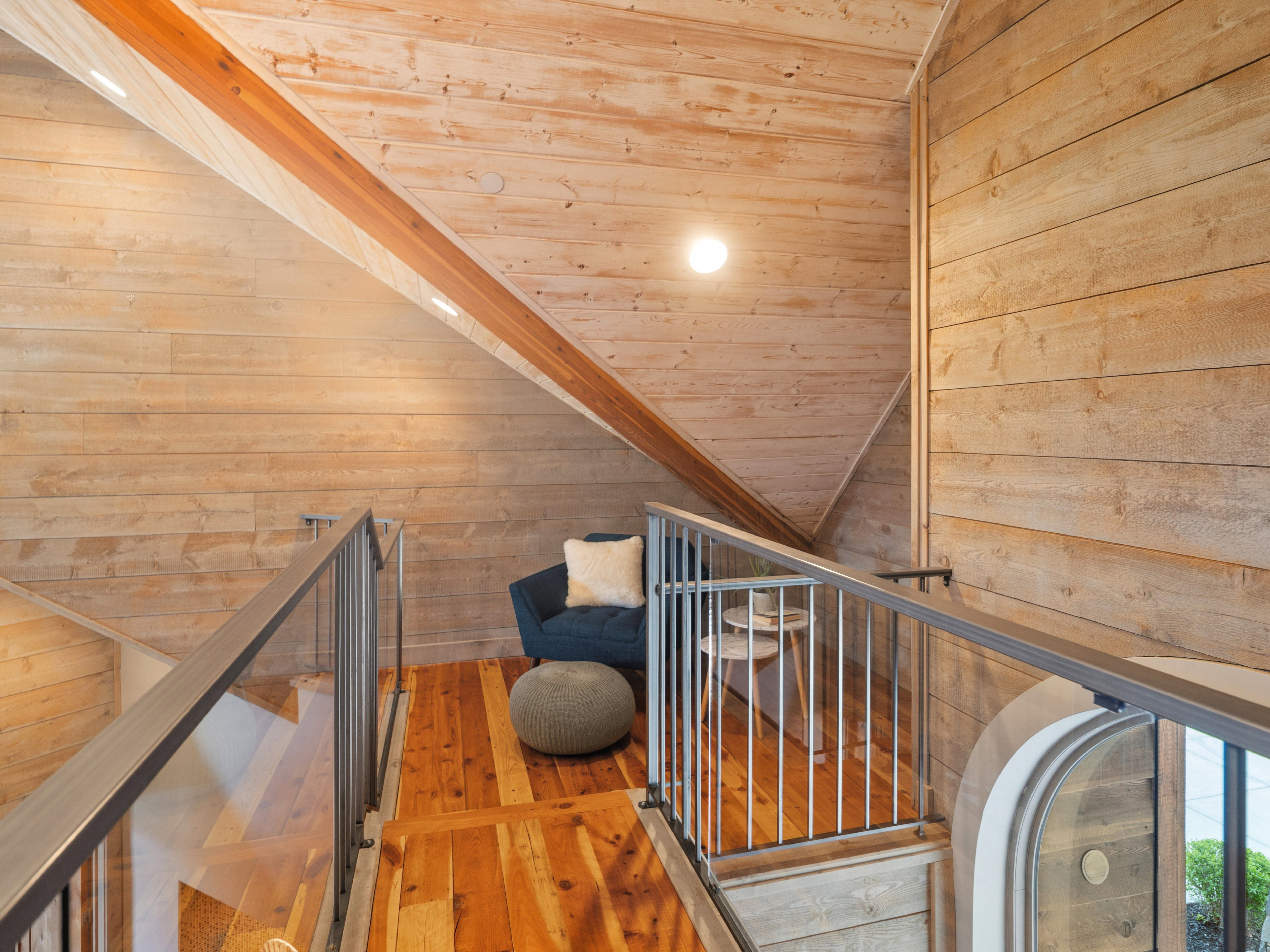 Attic loft featuring wood-plank walls and ceiling, wood-finish flooring, exposed wood beam, metal and glass railing, and a vaulted ceiling with recessed lighting