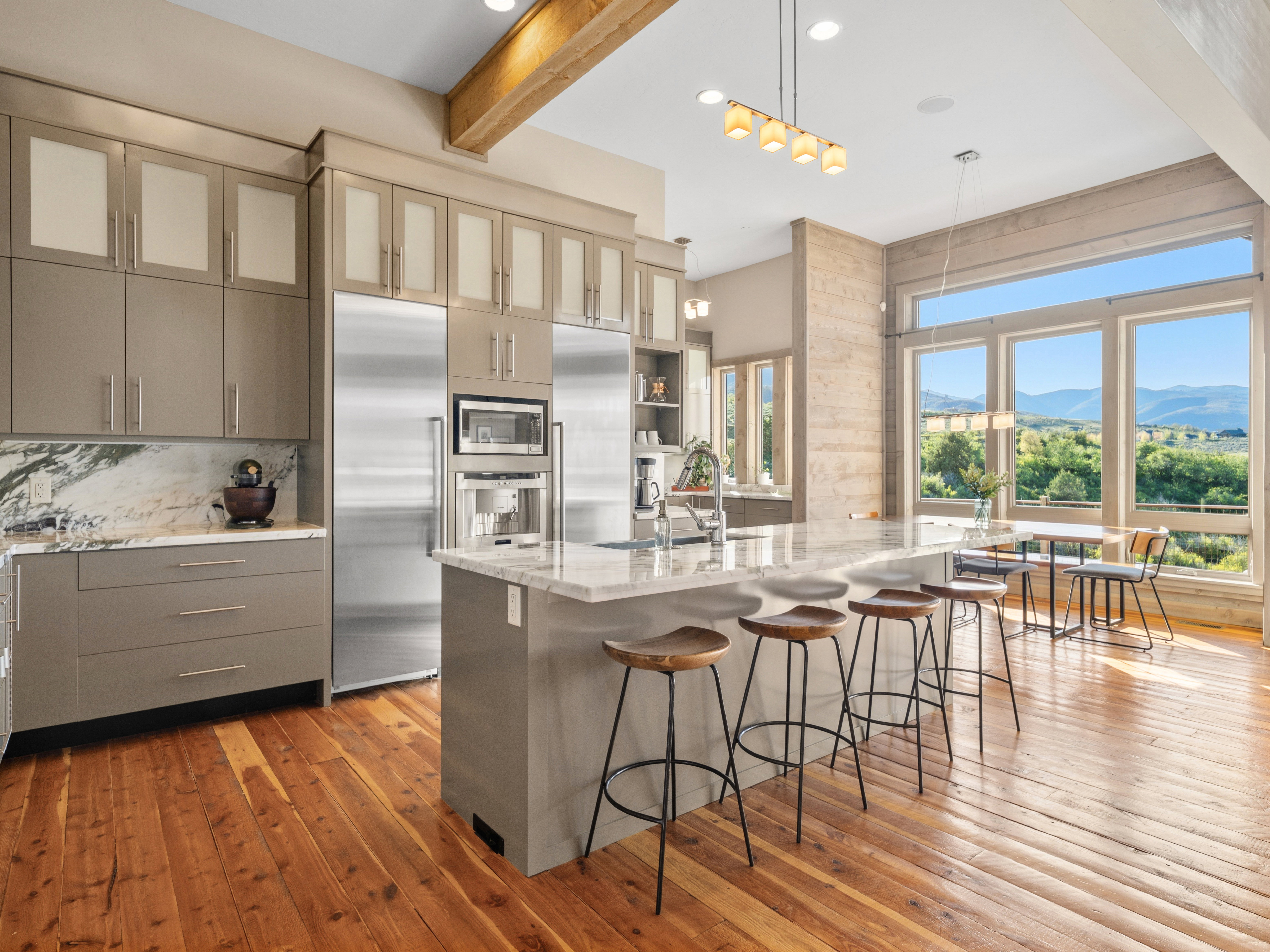 Kitchen featuring large windows, wood-finish flooring, a wood beam ceiling accent, stone countertops, and integrated stainless steel appliances