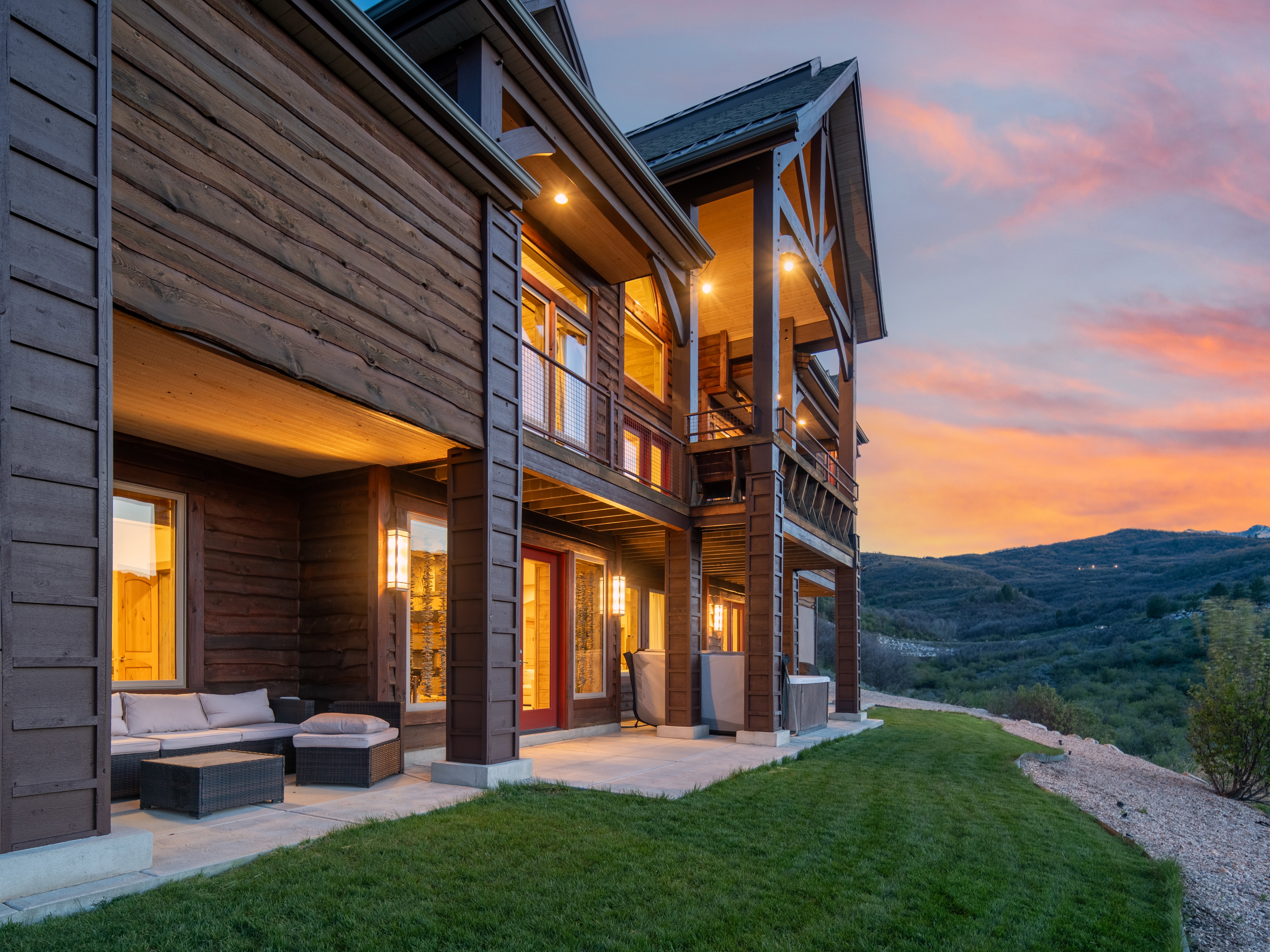 Multi-level wood-clad residence featuring an expansive ground-level patio, a covered upper balcony, and a manicured lawn