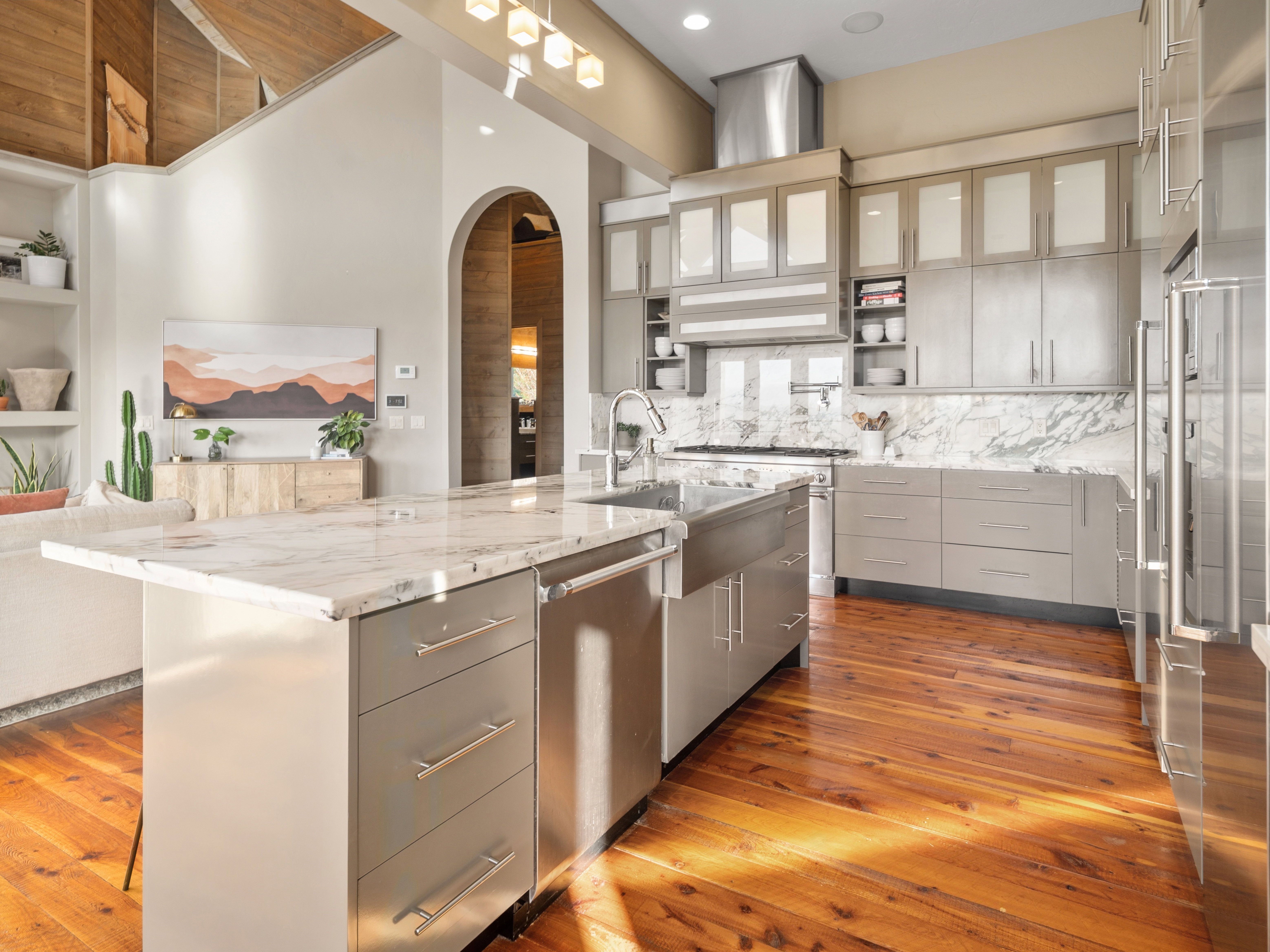 Open-concept kitchen featuring an oversized island with an undermount sink, stainless steel appliances, light-toned cabinetry, and a stone slab backsplash