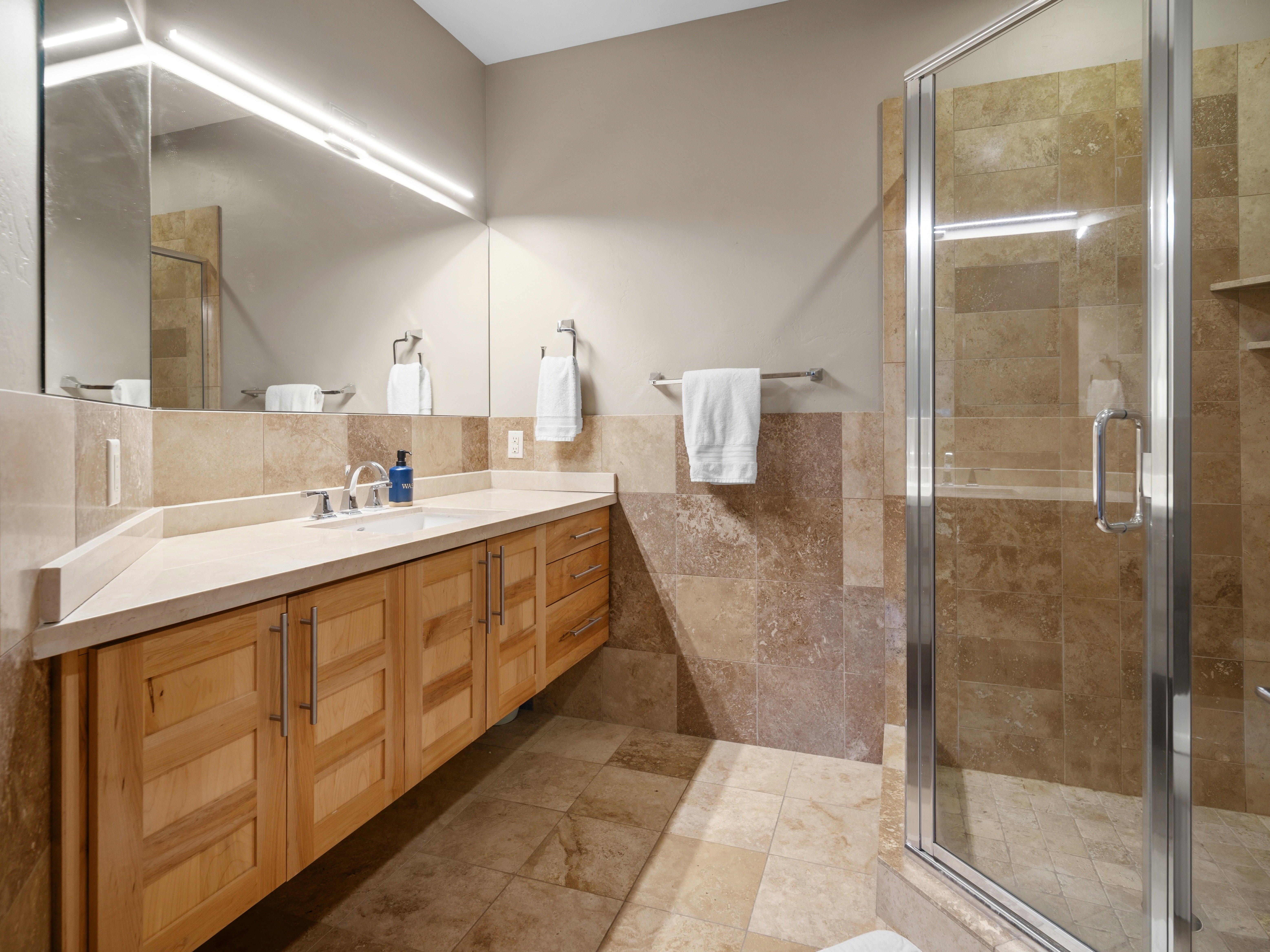 Bathroom featuring a wood-finish vanity with a light-toned countertop, an integrated sink, and a large wall-mounted mirror