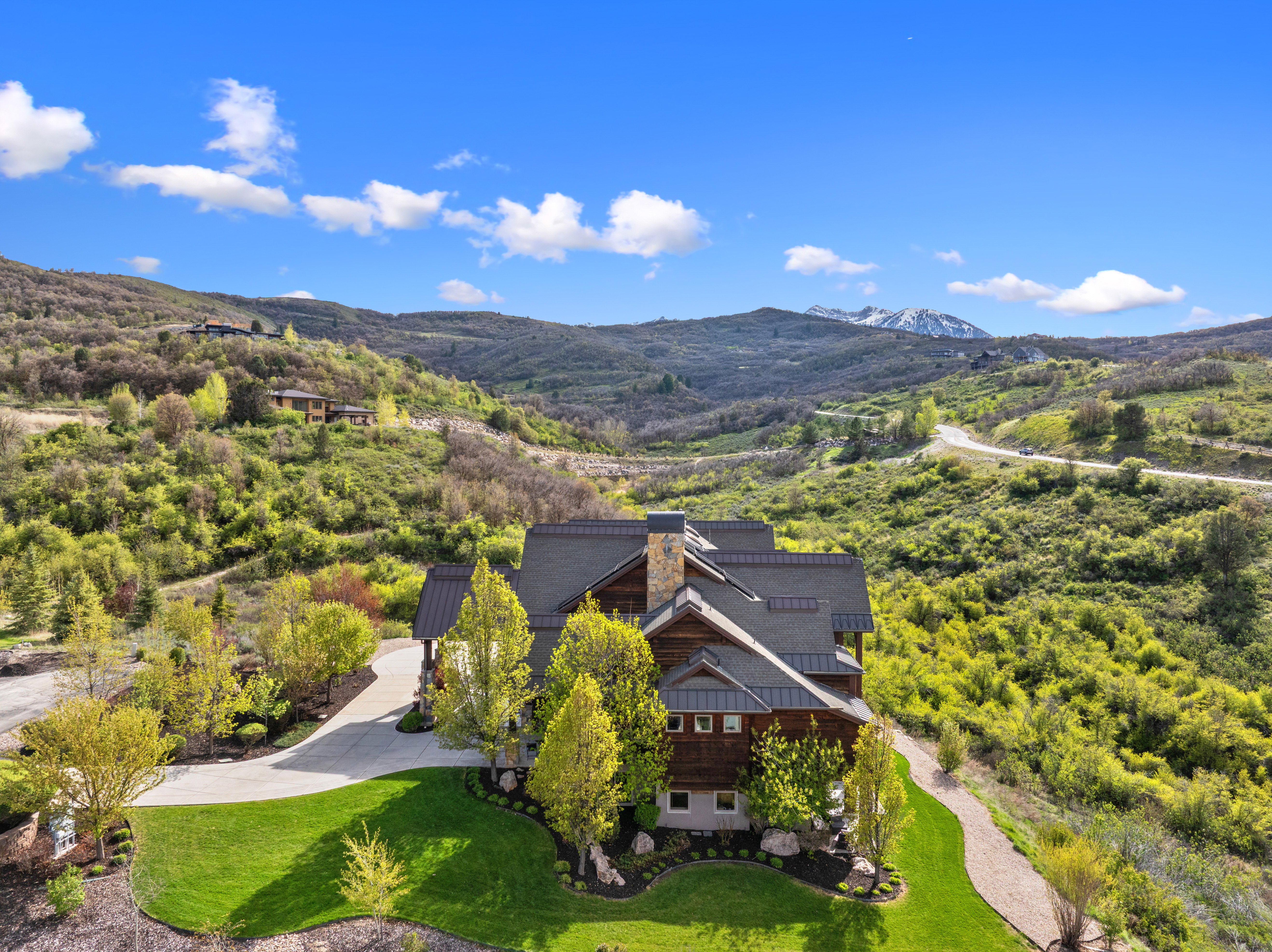 Expansive mountain-side residence featuring a multi-level roofline, stone chimney, wood siding, and mature landscaping