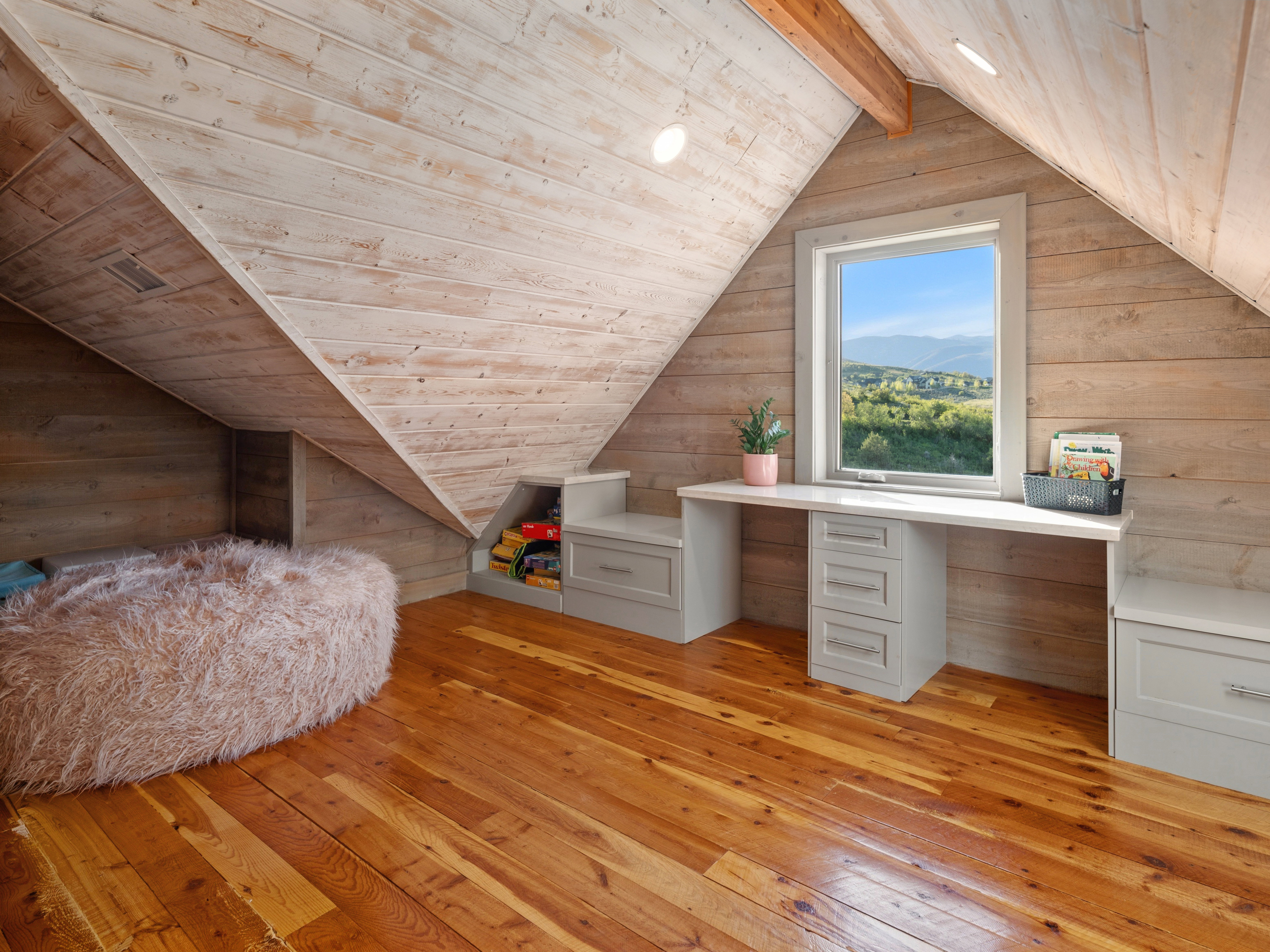 Vaulted attic space featuring wood-finish flooring, wood plank walls, and a built-in desk with drawers