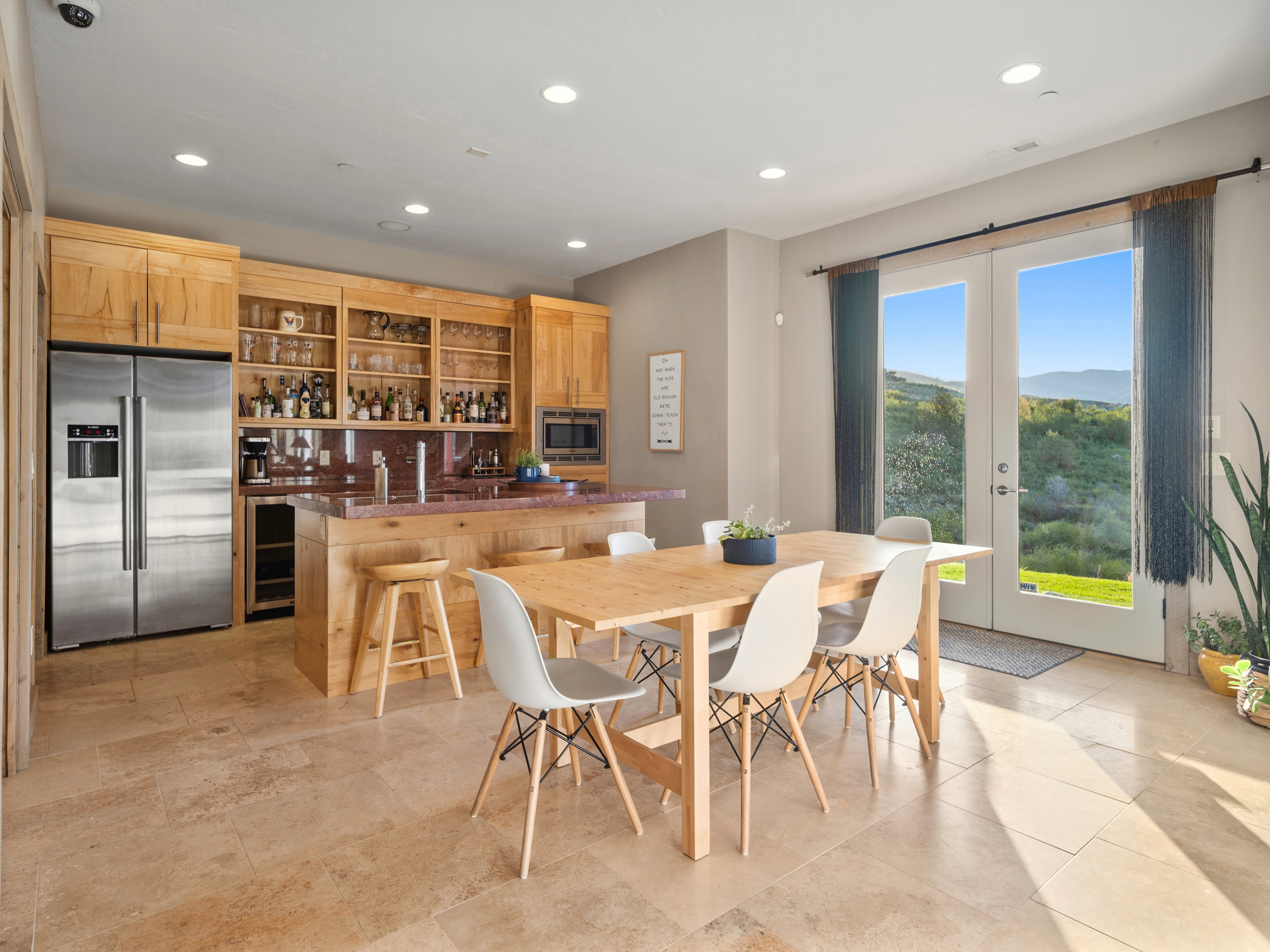 Spacious room featuring light-toned tile flooring, a custom wood wet bar with integrated shelving, stainless steel refrigerator, and built-in microwave