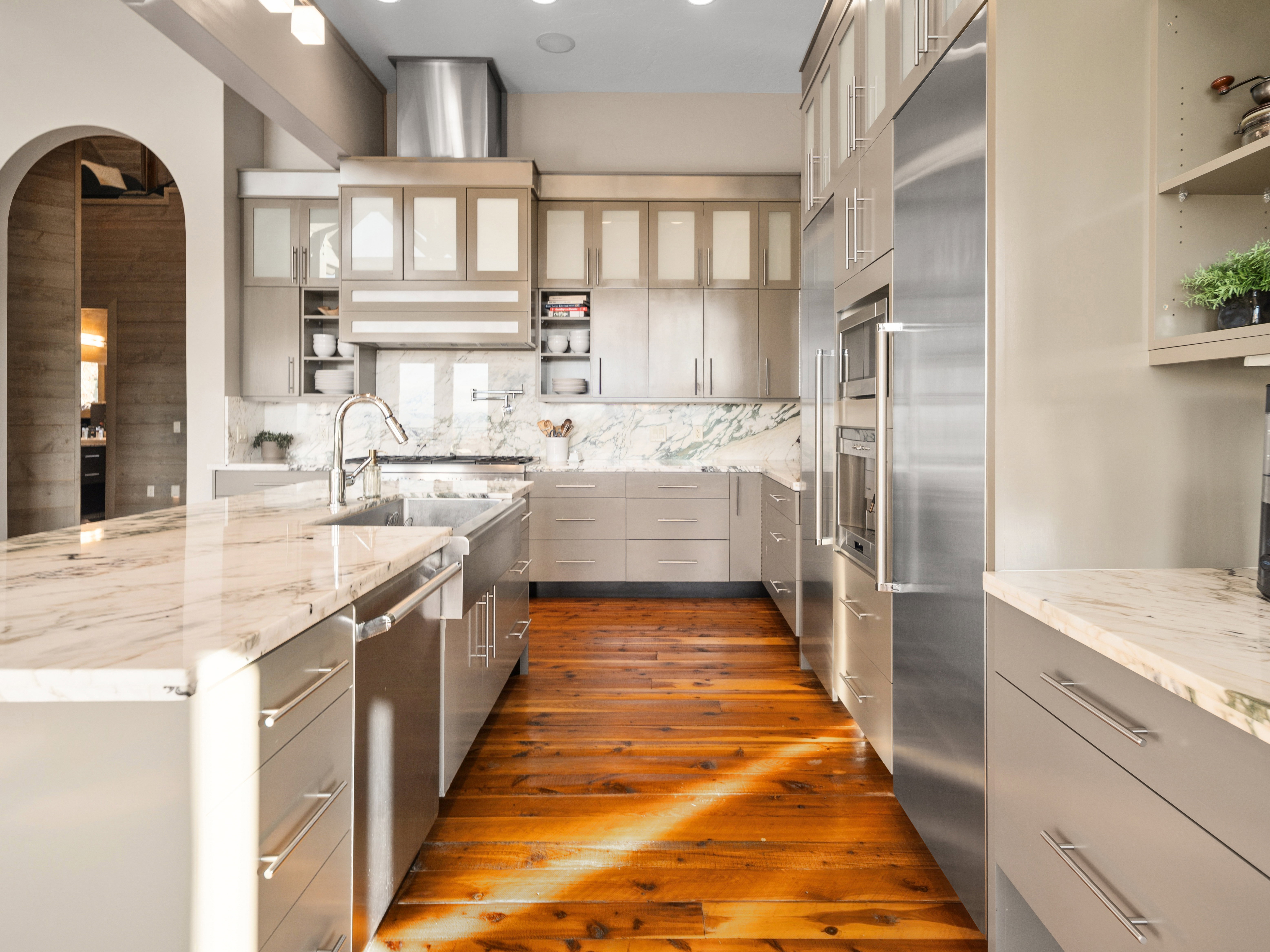 Gourmet kitchen featuring a large island with an undermount sink, stone countertops, integrated stainless steel appliances, contemporary cabinetry, and wood-finish flooring