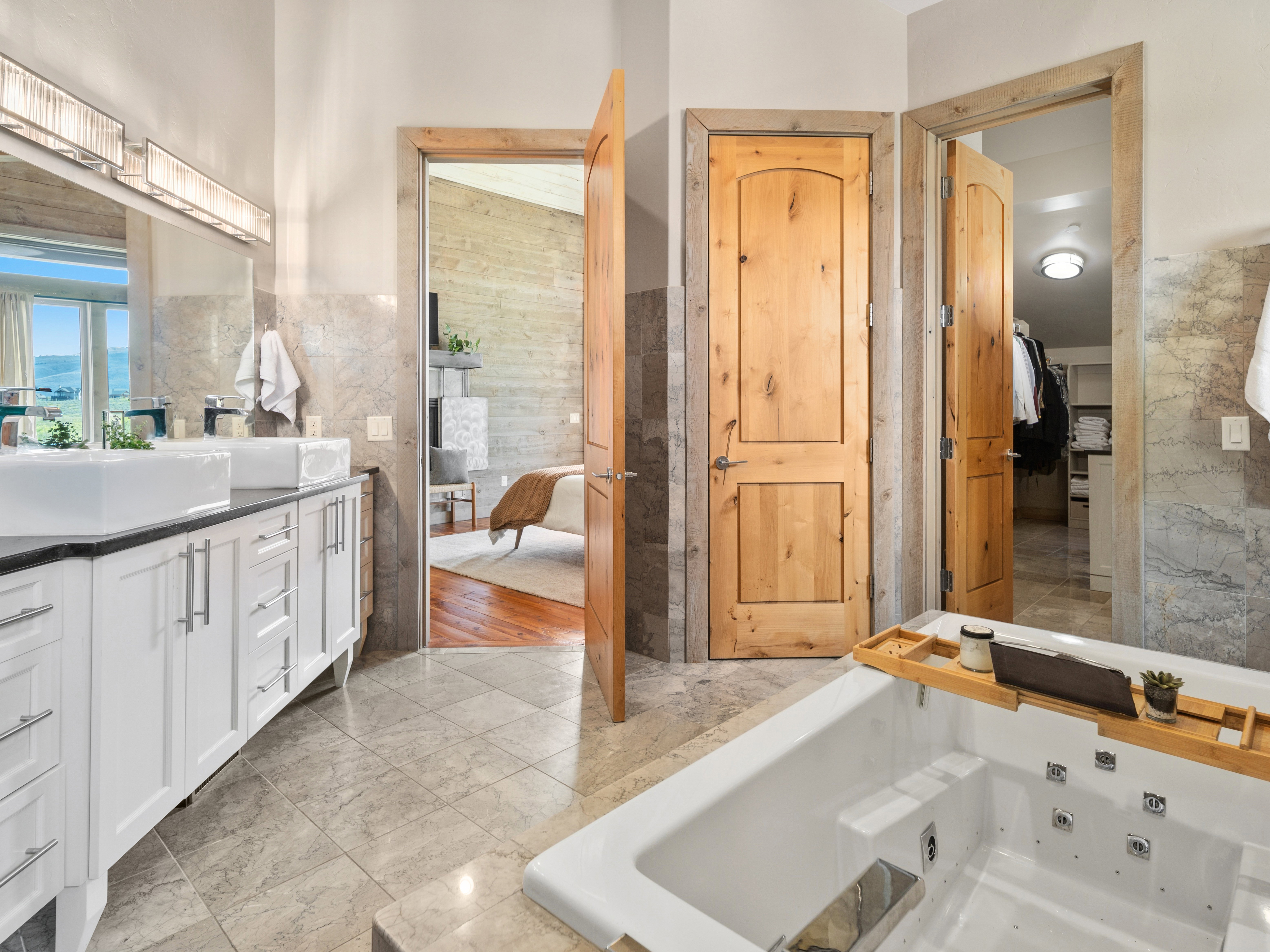 Spacious bathroom featuring a built-in jetted tub, dual vessel sinks, a vanity with ample storage, and stone tile flooring