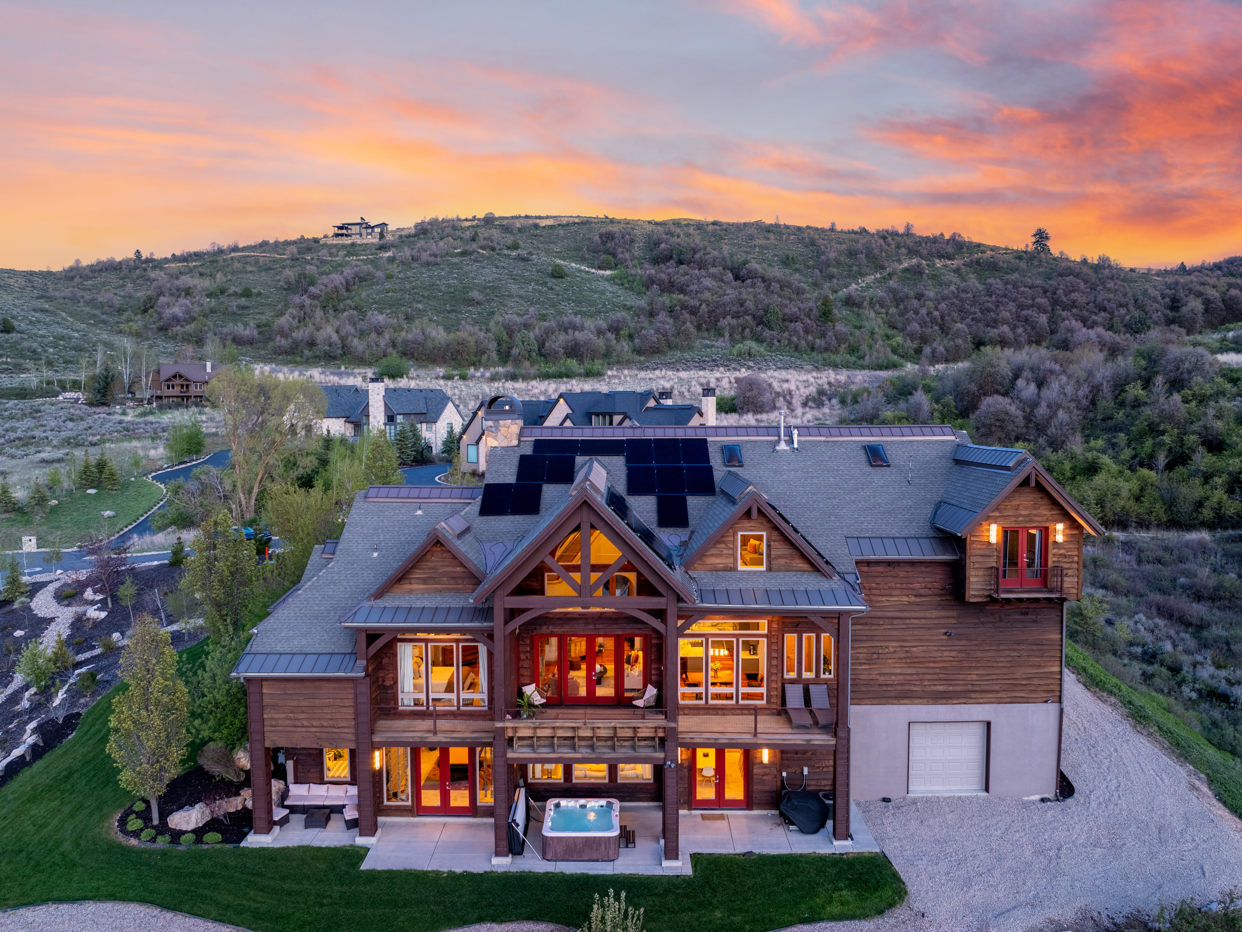 Multi-level mountain-style residence featuring a wood and stone exterior, multiple balconies, a lower-level patio with an integrated spa, and rooftop solar panels