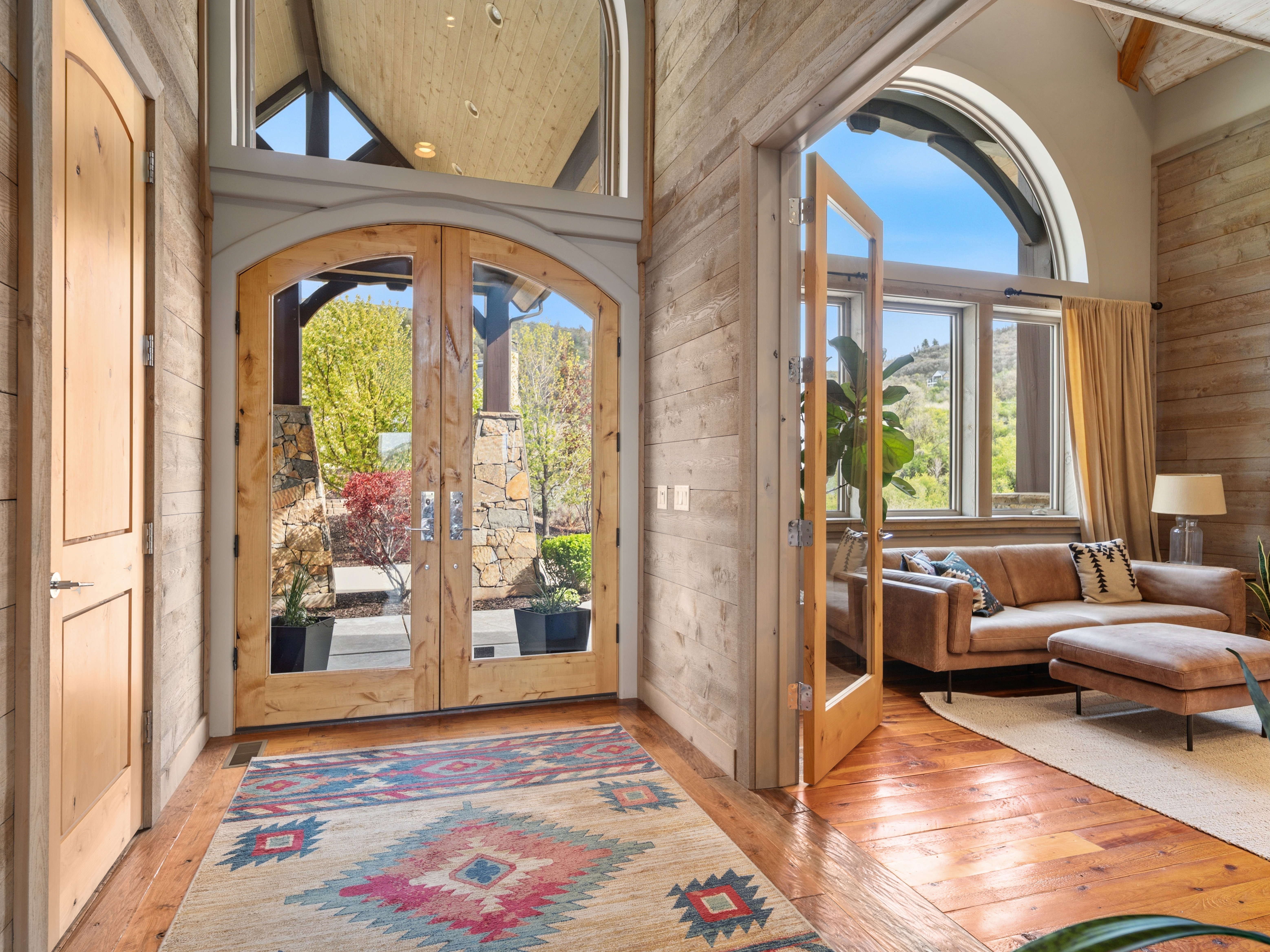 Arched glass-paneled entry doors with a transom window open to a foyer with wood-finish flooring and plank walls