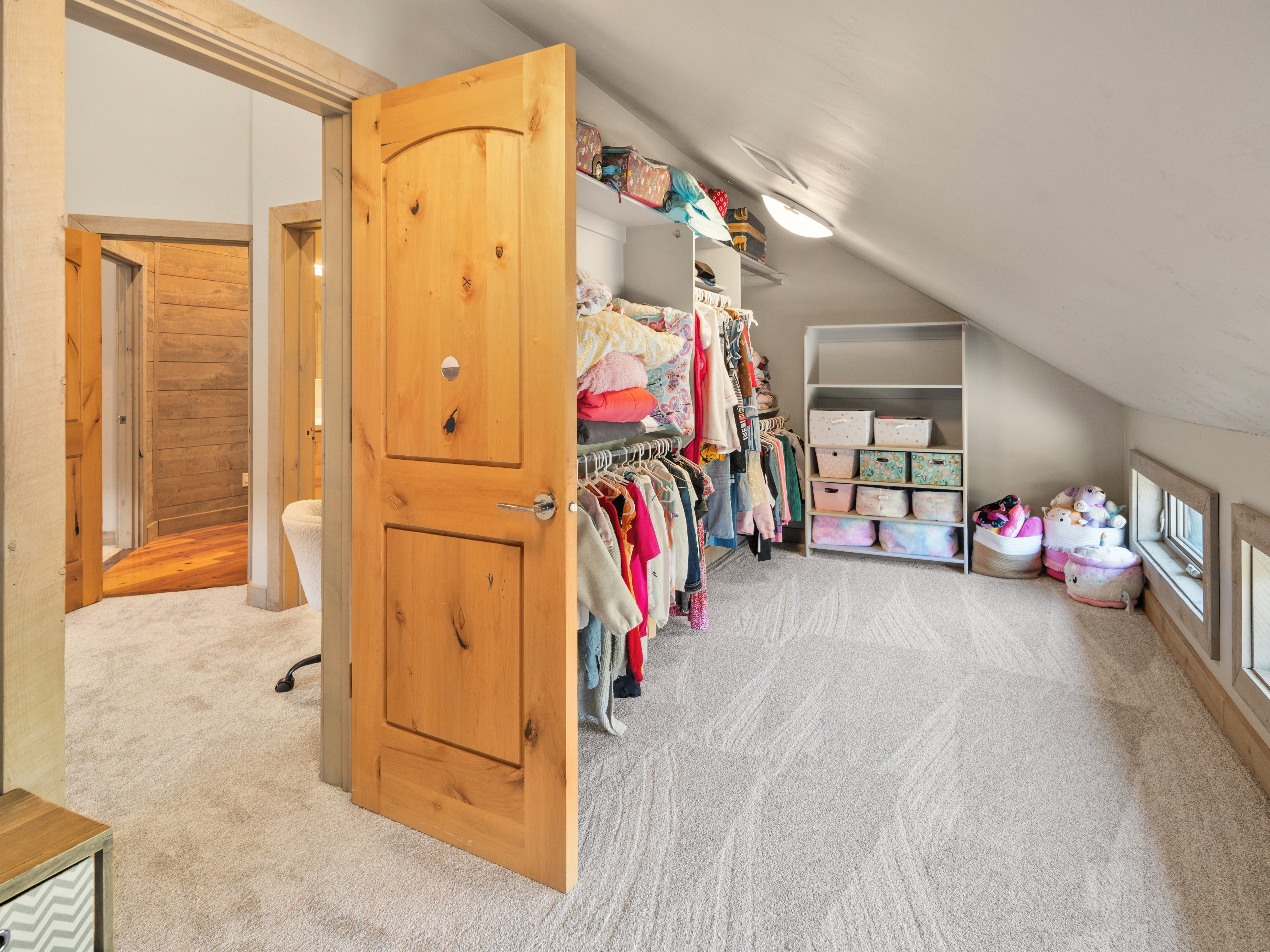 Carpeted attic space featuring sloped ceilings, built-in shelving, and multiple windows with wood trim