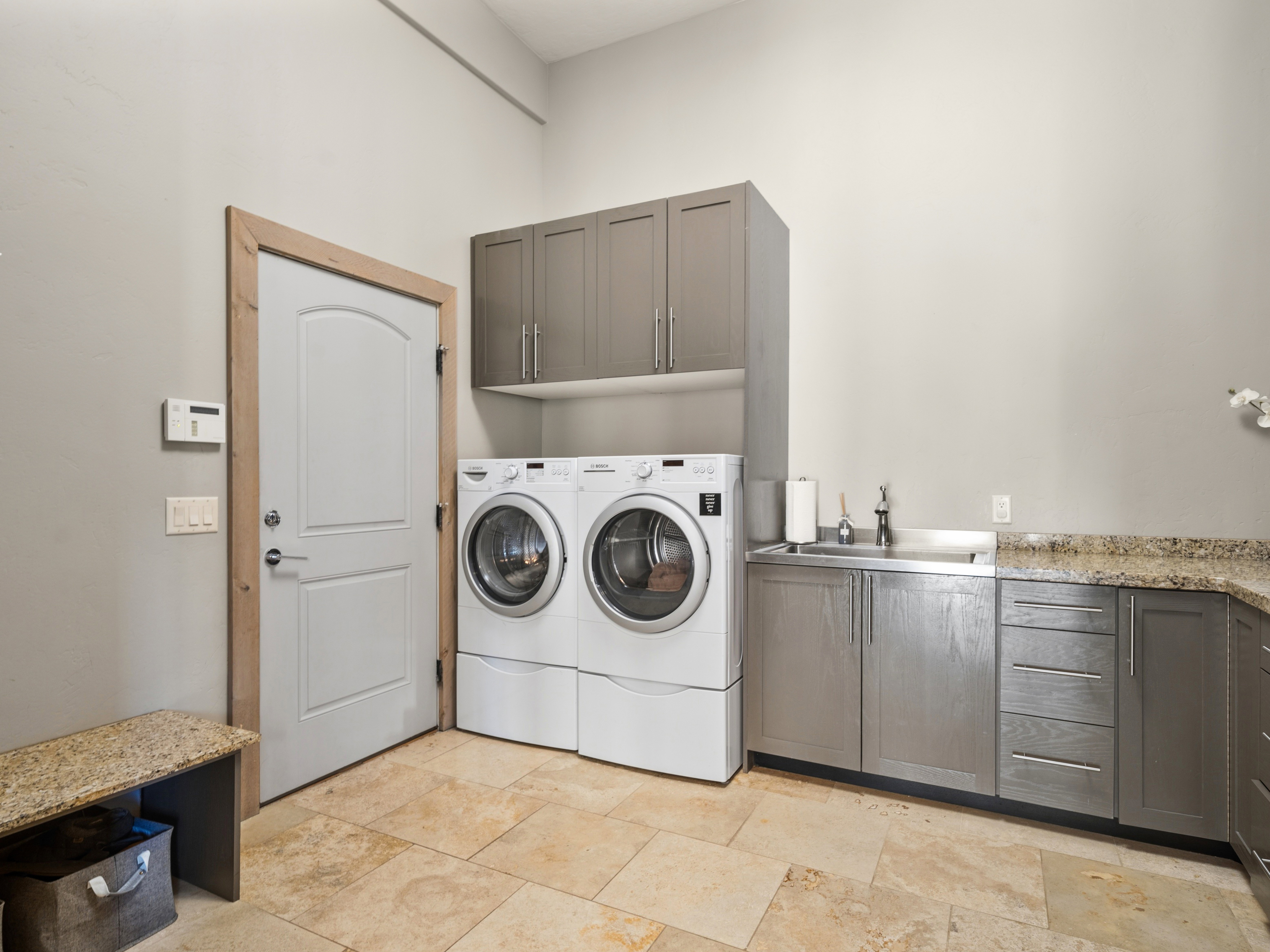 Laundry area featuring light-toned tile flooring, gray cabinetry, and stone-finish countertops