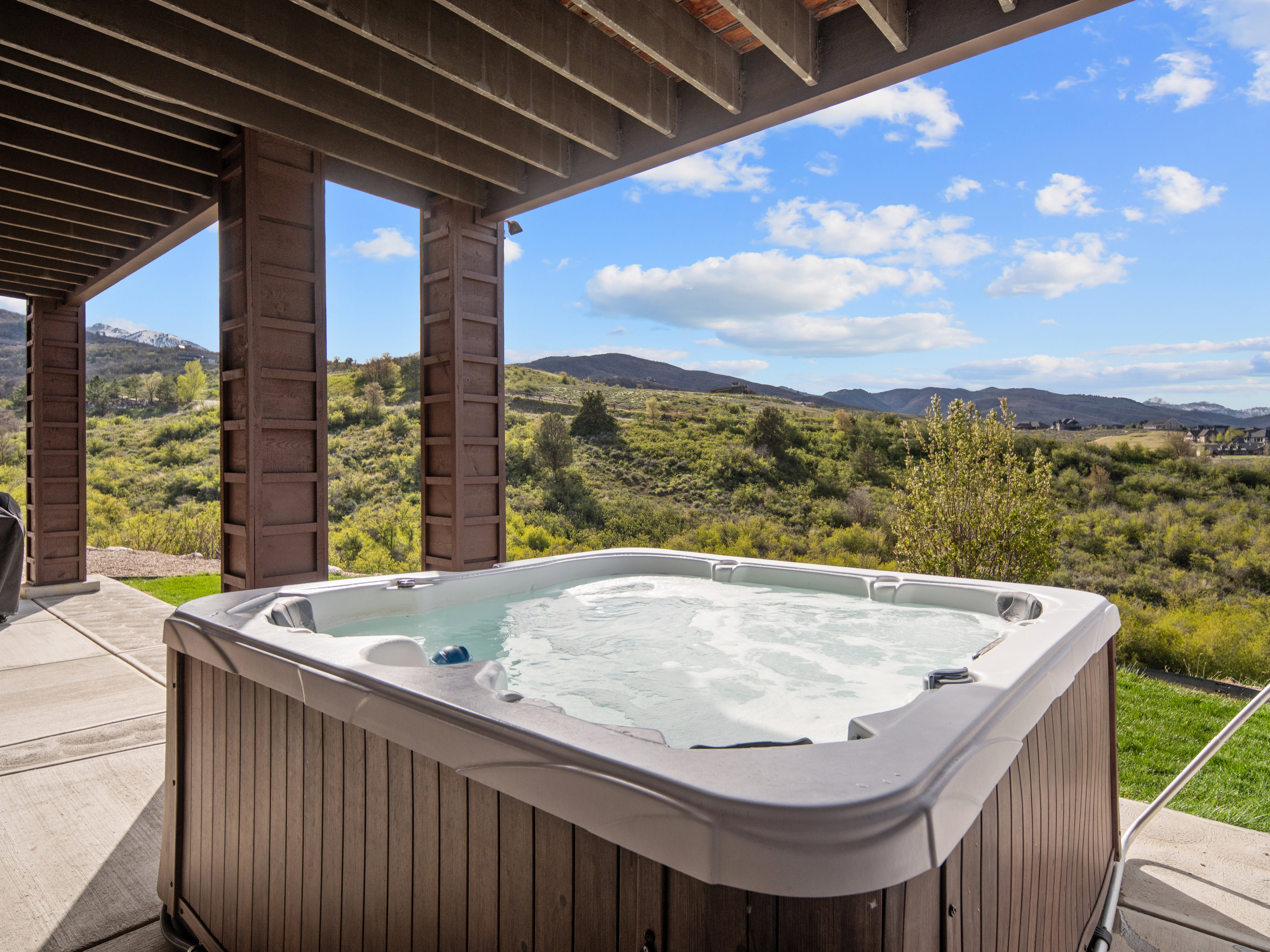 Outdoor spa tub with wood-finish siding situated on a concrete patio, offering expansive mountain scenery