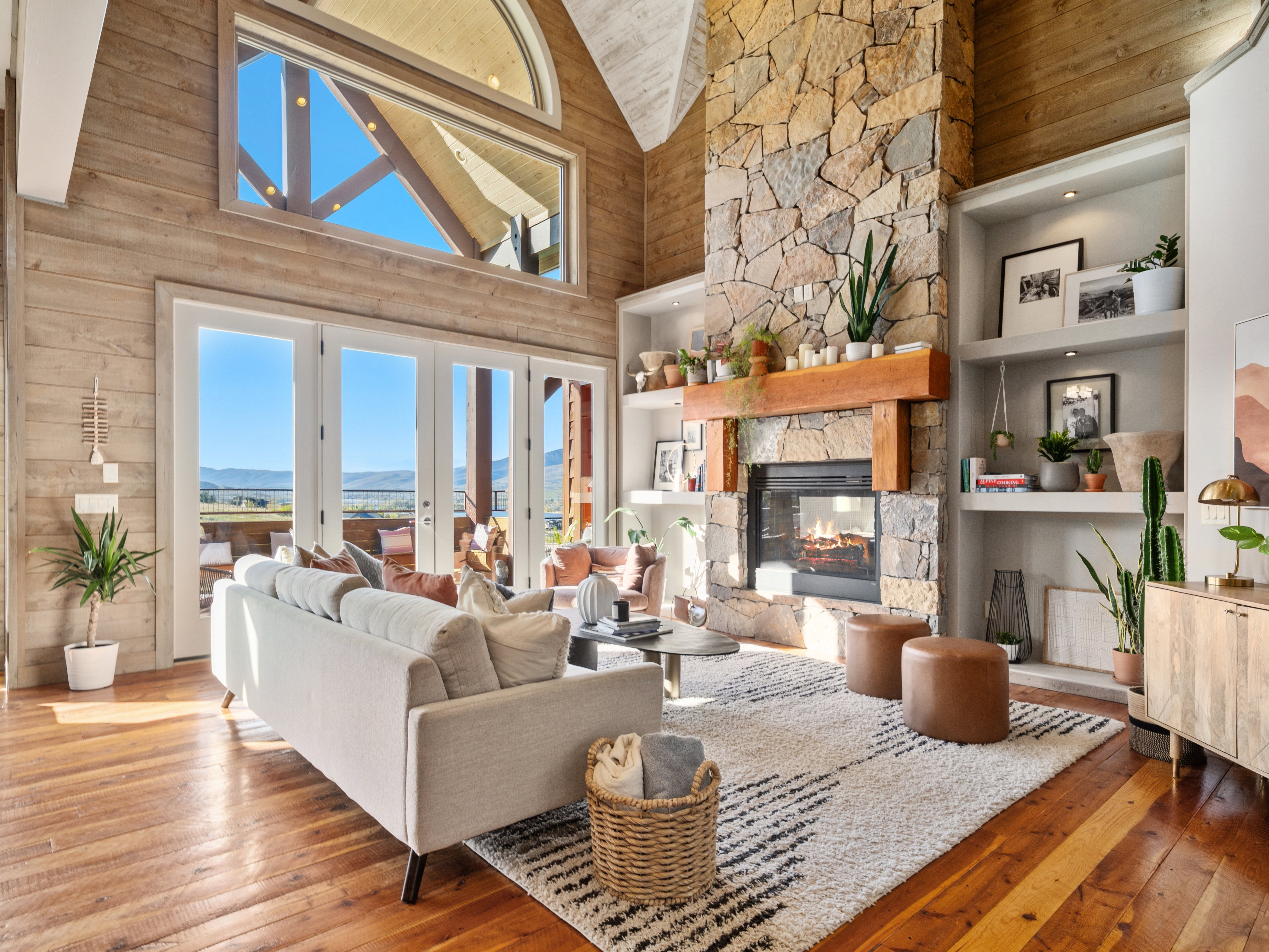 Spacious living area featuring a stone fireplace, wood-finish flooring, and exposed wood ceiling beams