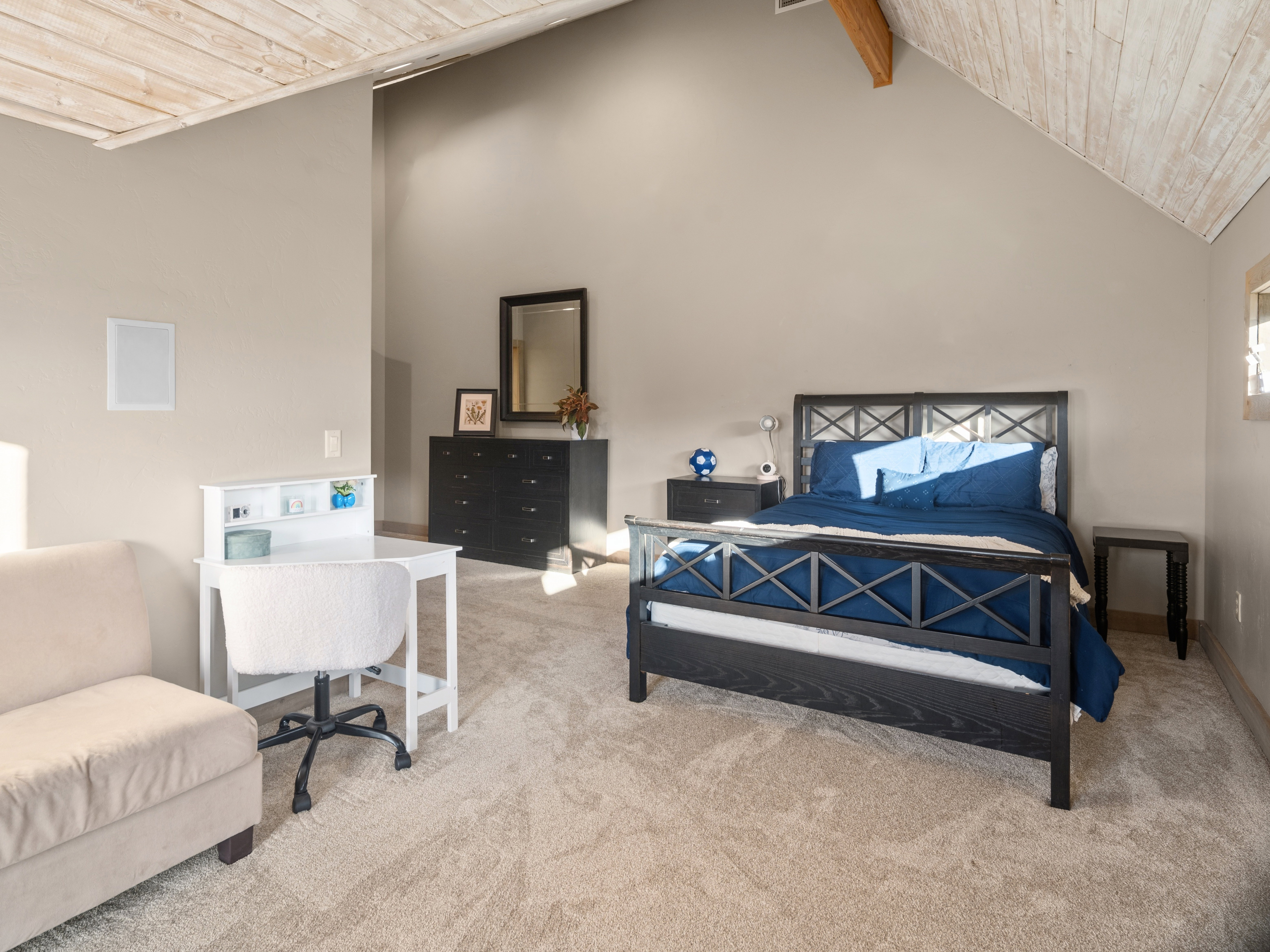 Vaulted wood-paneled ceiling with exposed wood beam, neutral-toned walls, and plush carpet flooring