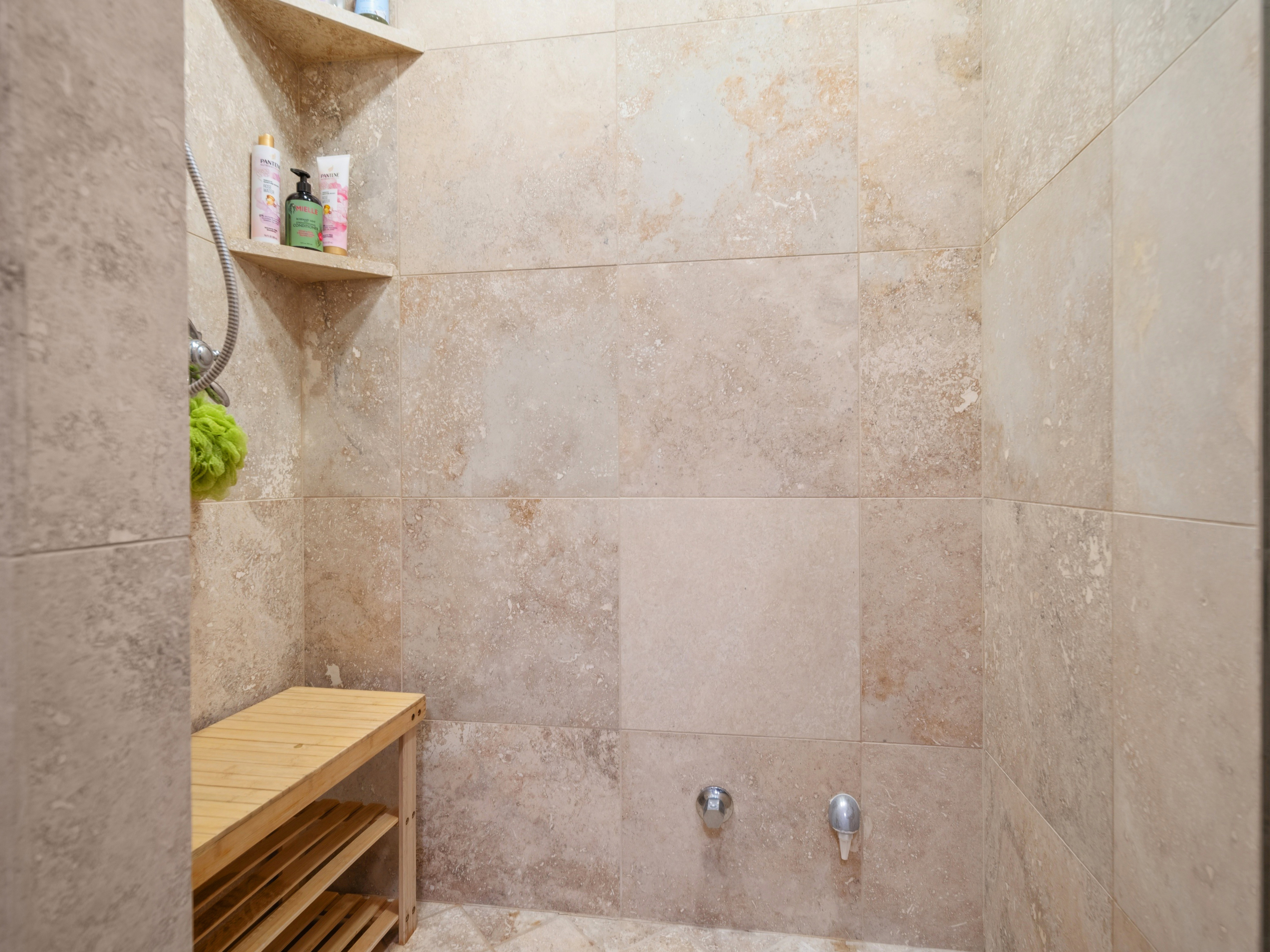 Tiled shower enclosure featuring integrated corner shelves and a built-in wooden bench