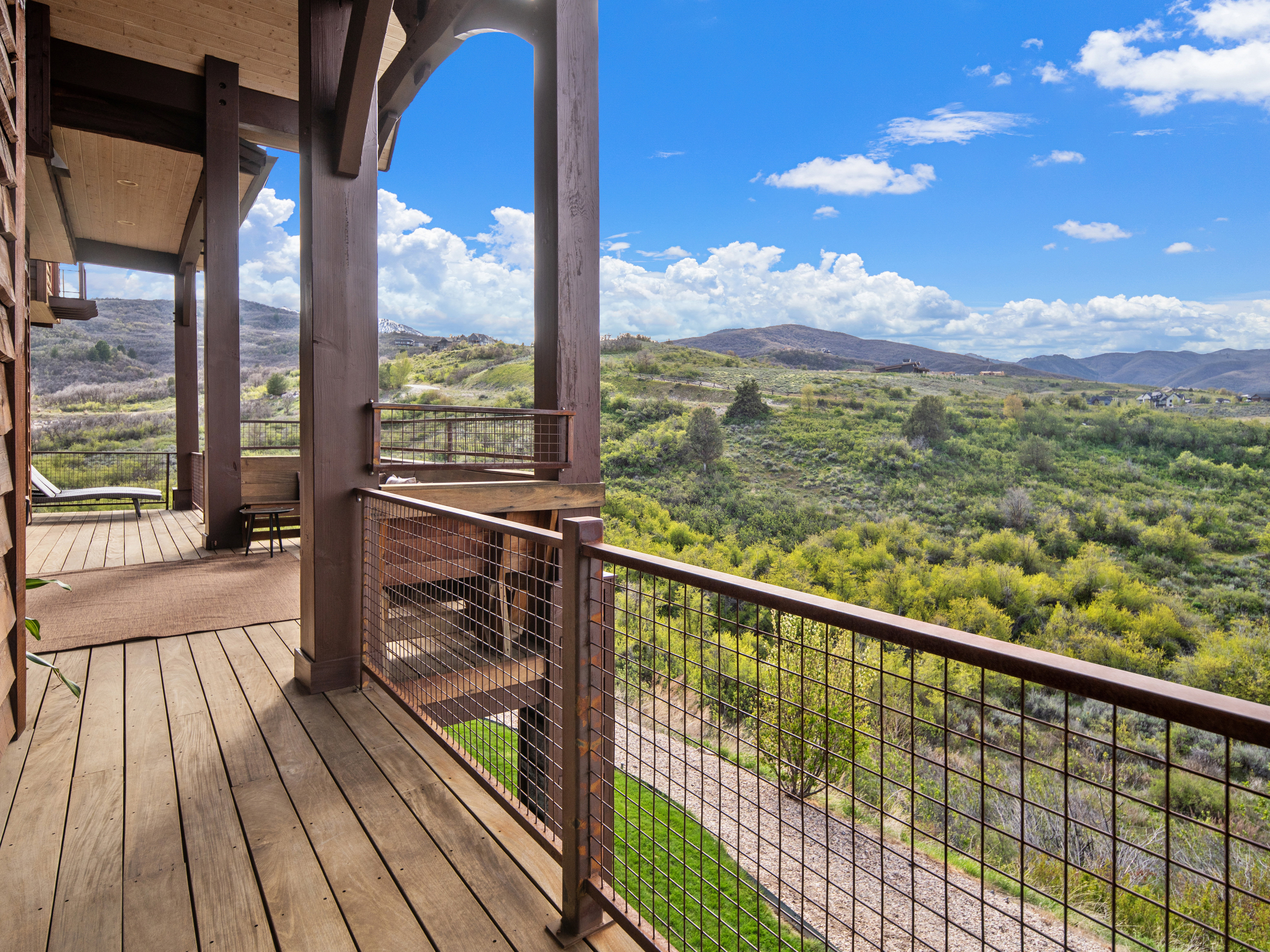 Expansive deck featuring wood flooring and a sturdy metal railing overlooking a vast, verdant landscape