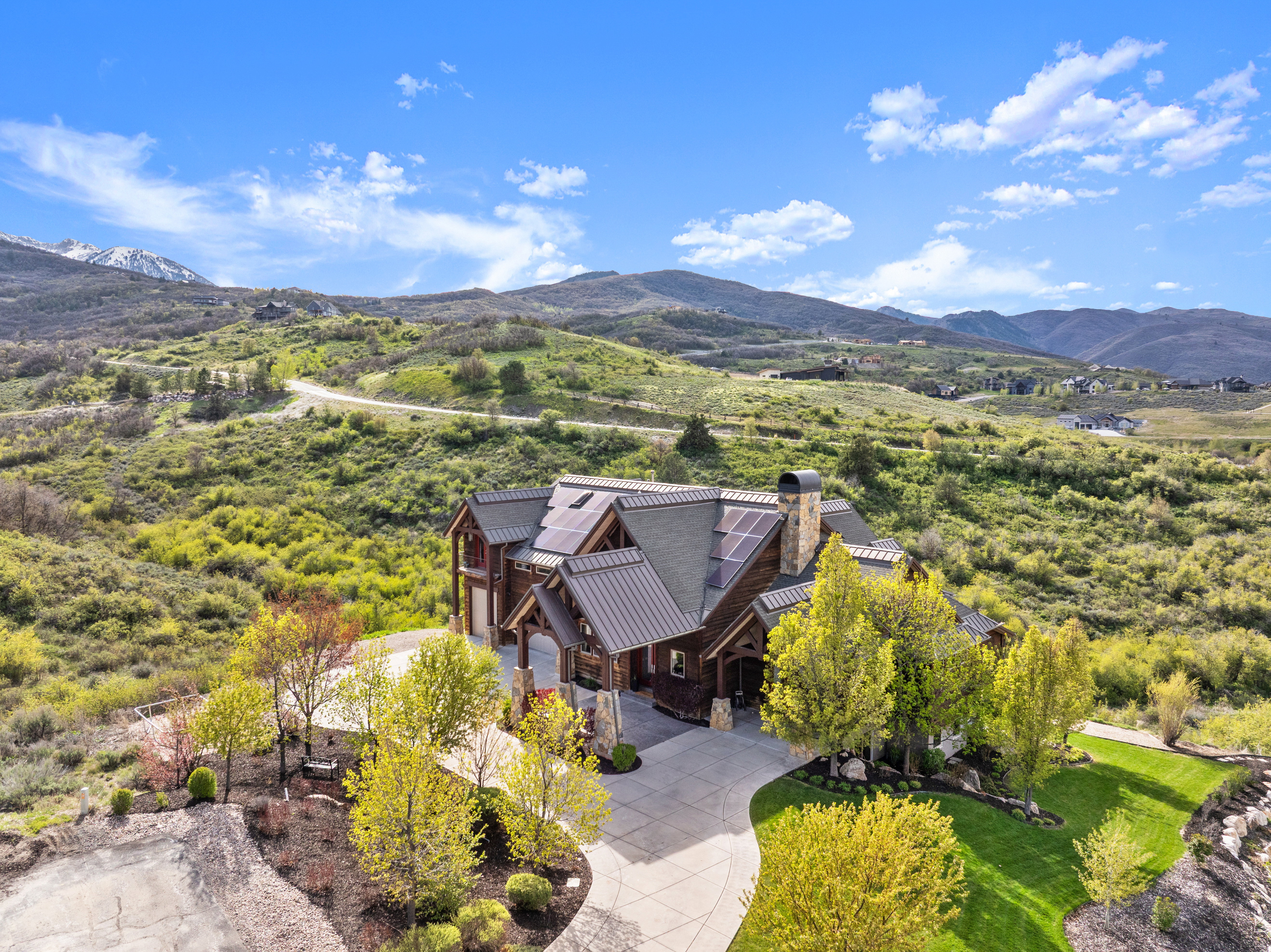 Mountain contemporary residence featuring a multi-gabled roofline with solar panels, a stone chimney, and a concrete driveway